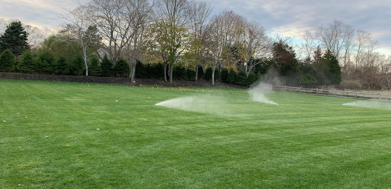 In-ground sprinkler watering a lush green lawn at dusk