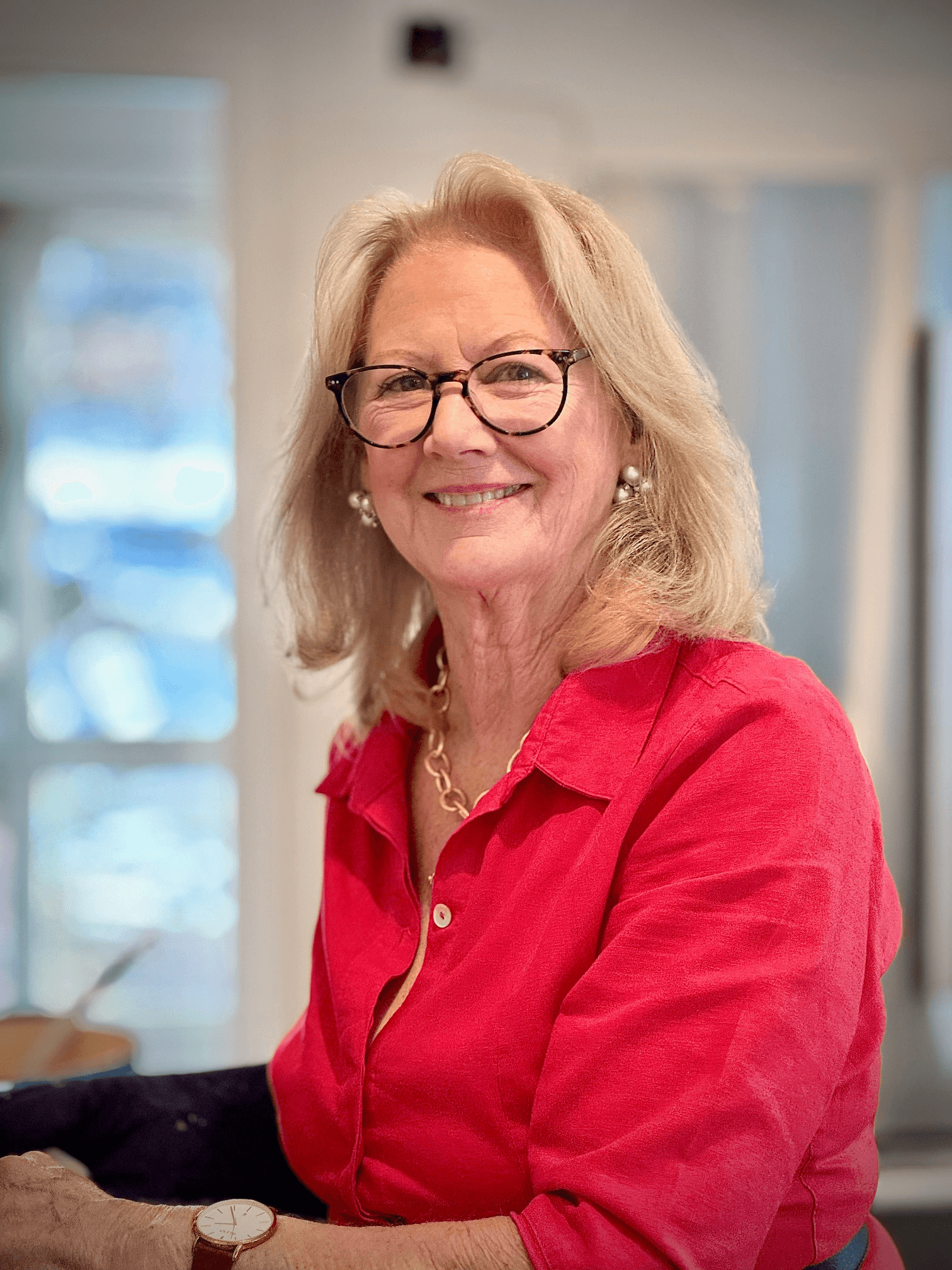 A woman with glasses in a red shirt sits at a desk, reflecting on her experiences as an artist and author.