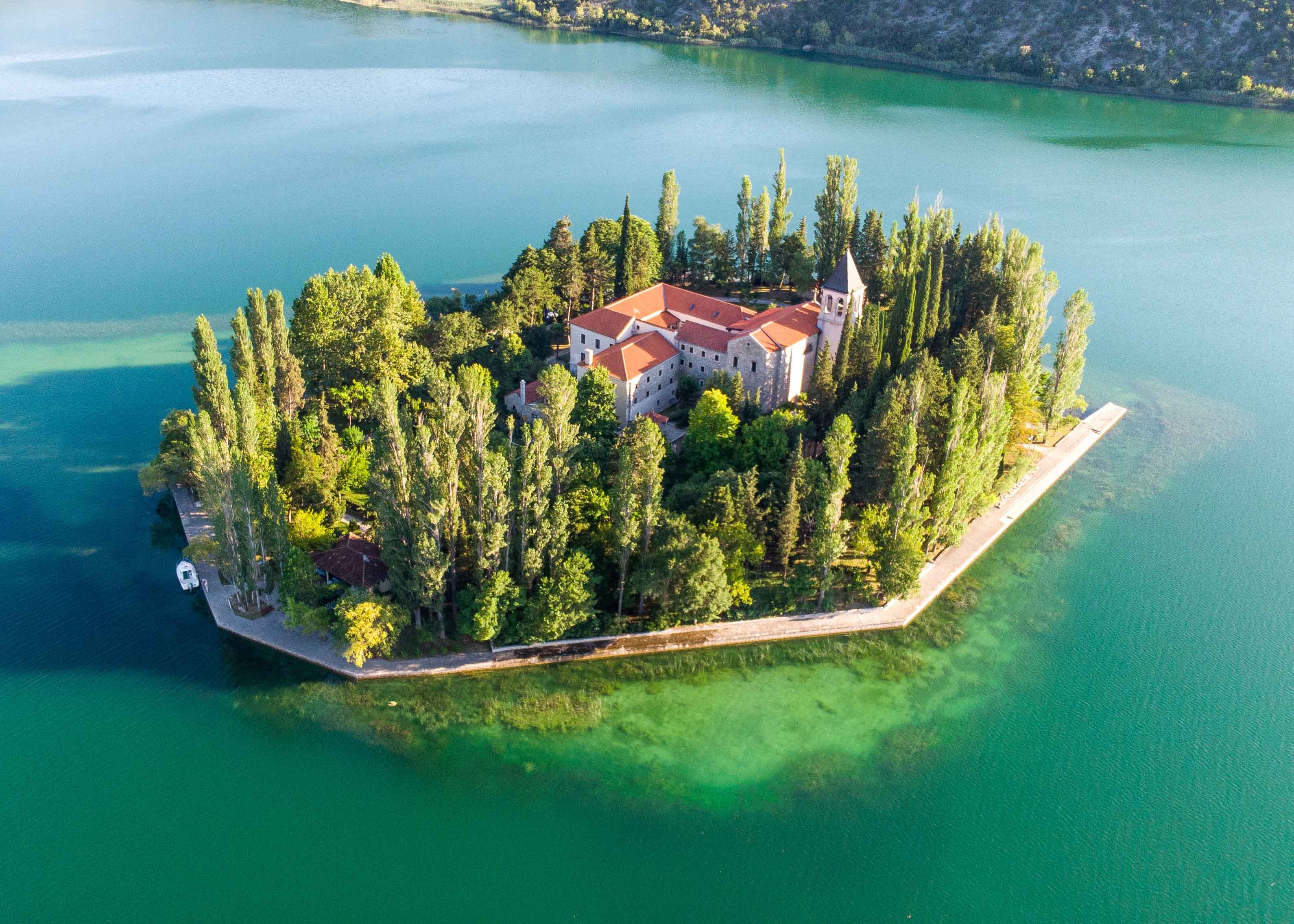 Aerial view of Krka Monastery surrounded by lush trees and turquoise water in Croatia.