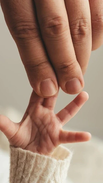 Tiny baby hand holding two adult fingers