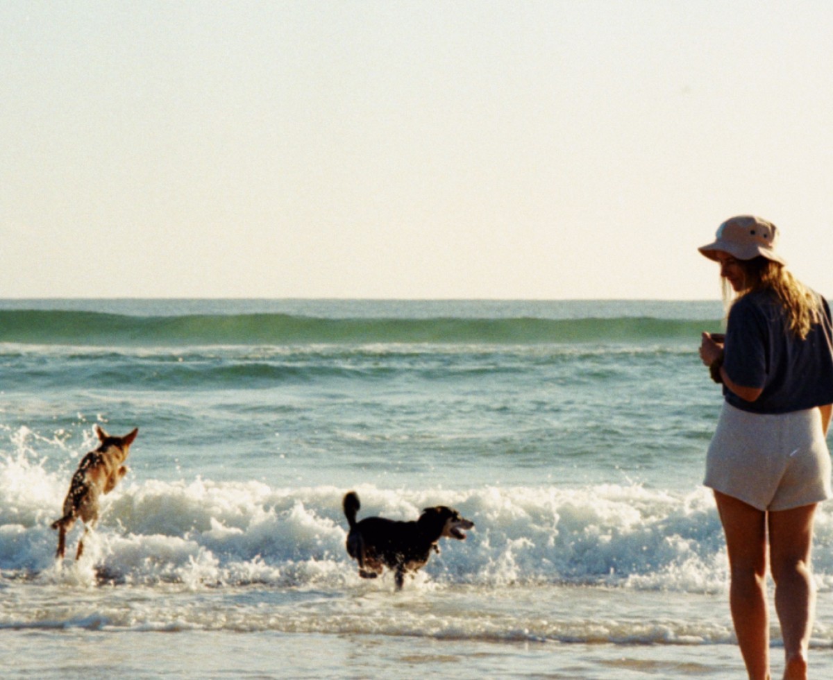 An image of the the founder of Hunde and her two dogs playing in the sea at the beach
