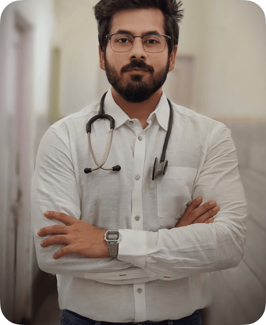 A confident individual in a white shirt with rolled-up sleeves stands in a corridor, wearing glasses and a stethoscope around their neck, conveying a professional demeanor.