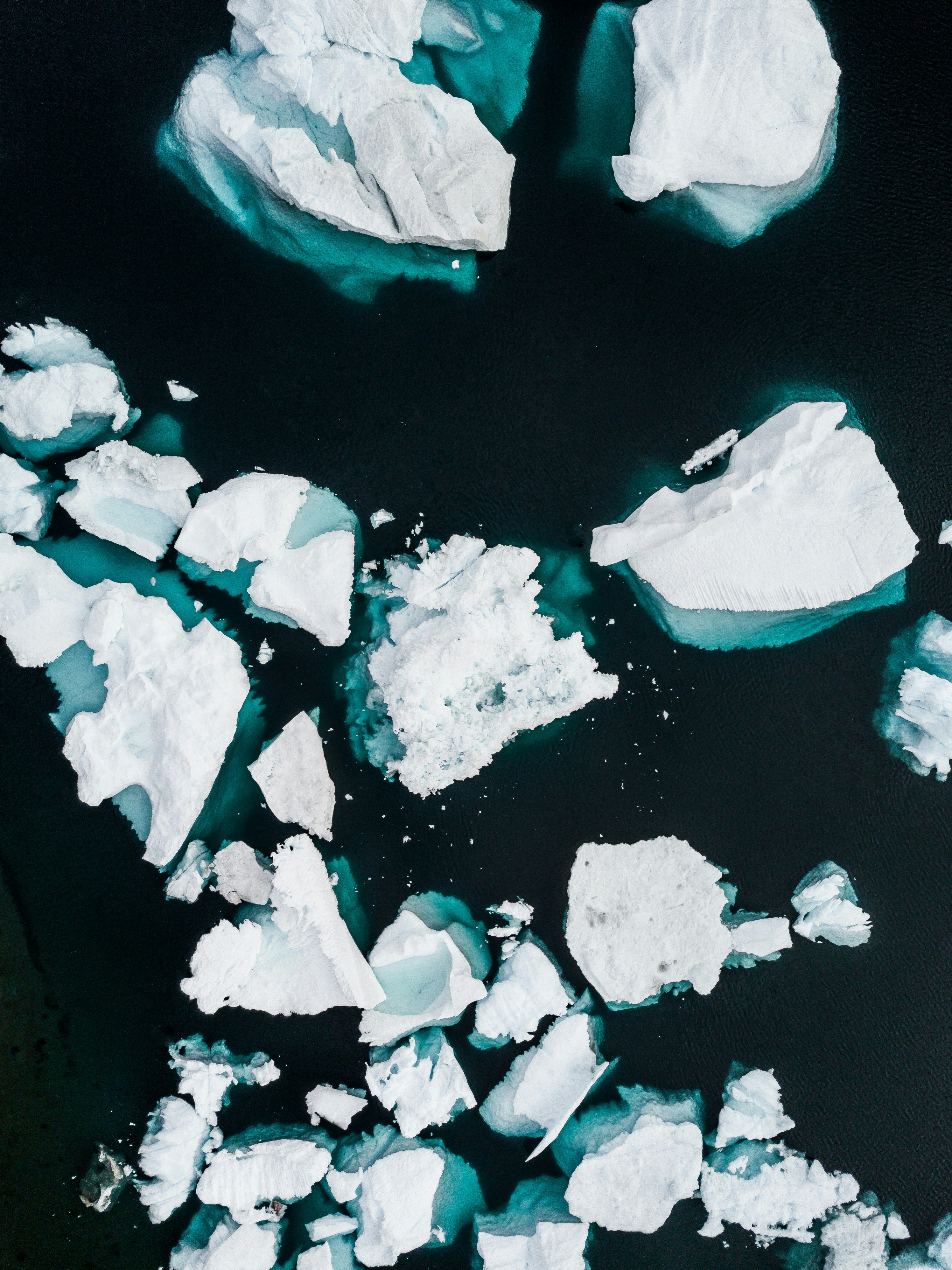 Aerial view of floating icebergs in dark waters, showcasing various shapes and sizes.