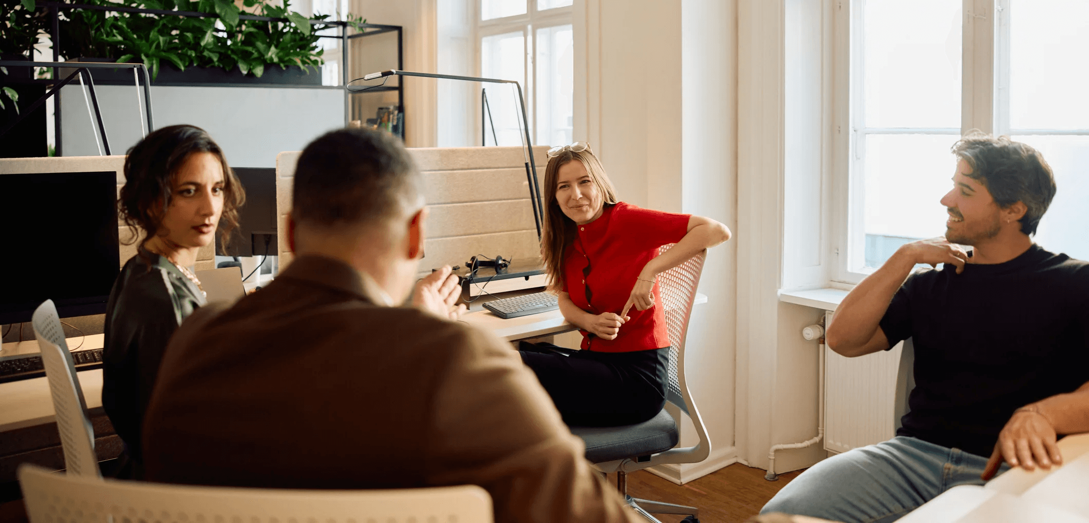 Woman in a tailored beige suit holding a structured brown leather handbag, standing in front of a softly lit modern background.