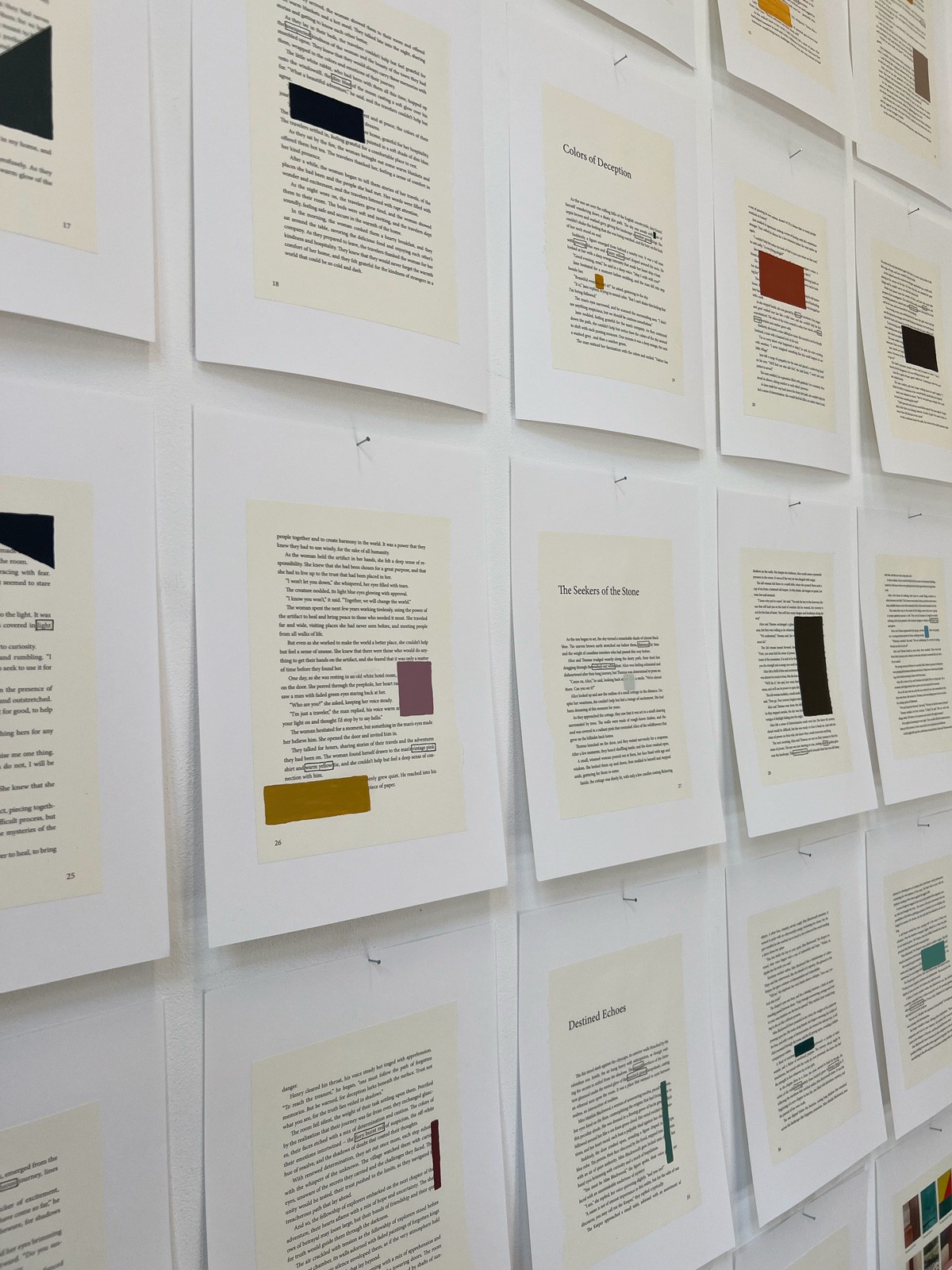 Een detailopname in perspectief van de muur met tekstvellen. De focus ligt op de textuur van het papier en de manier waarop de gekleurde vlakken over de tekst zijn geplaatst. Titels zoals "Colors of Deception" en "The Seekers of the Stone" zijn leesbaar.
