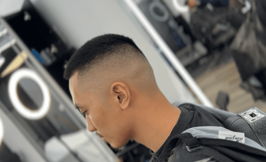 Man with short curly hair and a low fade on the sides, sitting in a barbershop chair.