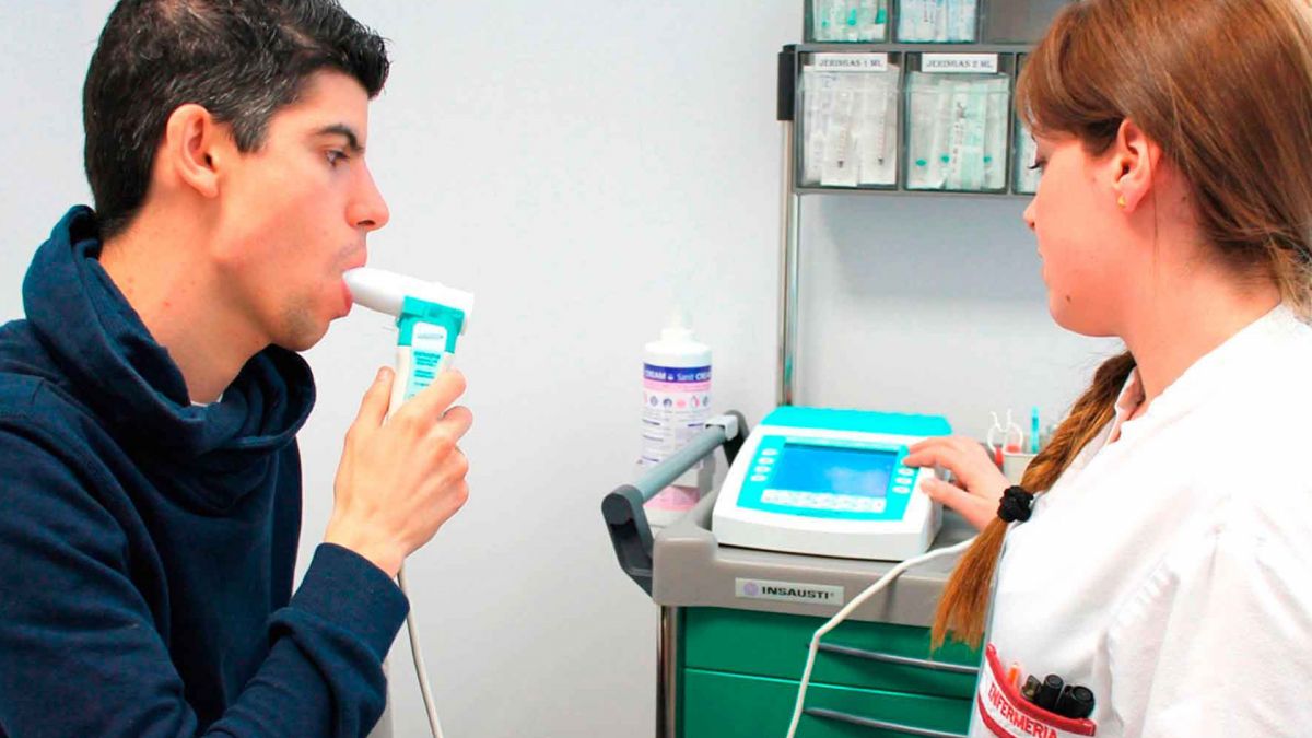 Paciente realizando prueba de espirometría asistido por profesional de salud con espirómetro digital