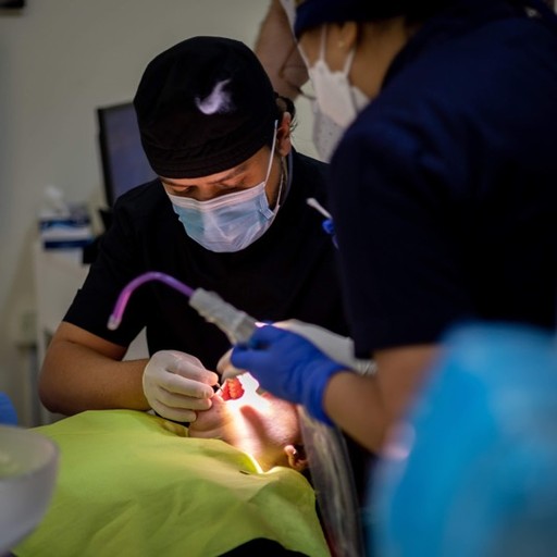 A dentist at Bella Medical Centre examines a patient’s teeth closely, with an assistant staff member nearby. 