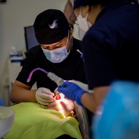 A dentist at Bella Medical Centre examines a patient’s teeth closely, with an assistant staff member nearby. 