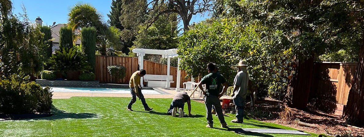 A crew of AGL Grass North installers is working hard on a residential backyard installation of artificial grass.