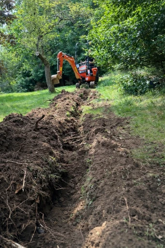 Mini digger excavating a trench in a residential garden for underground armoured cable installation in the UK.