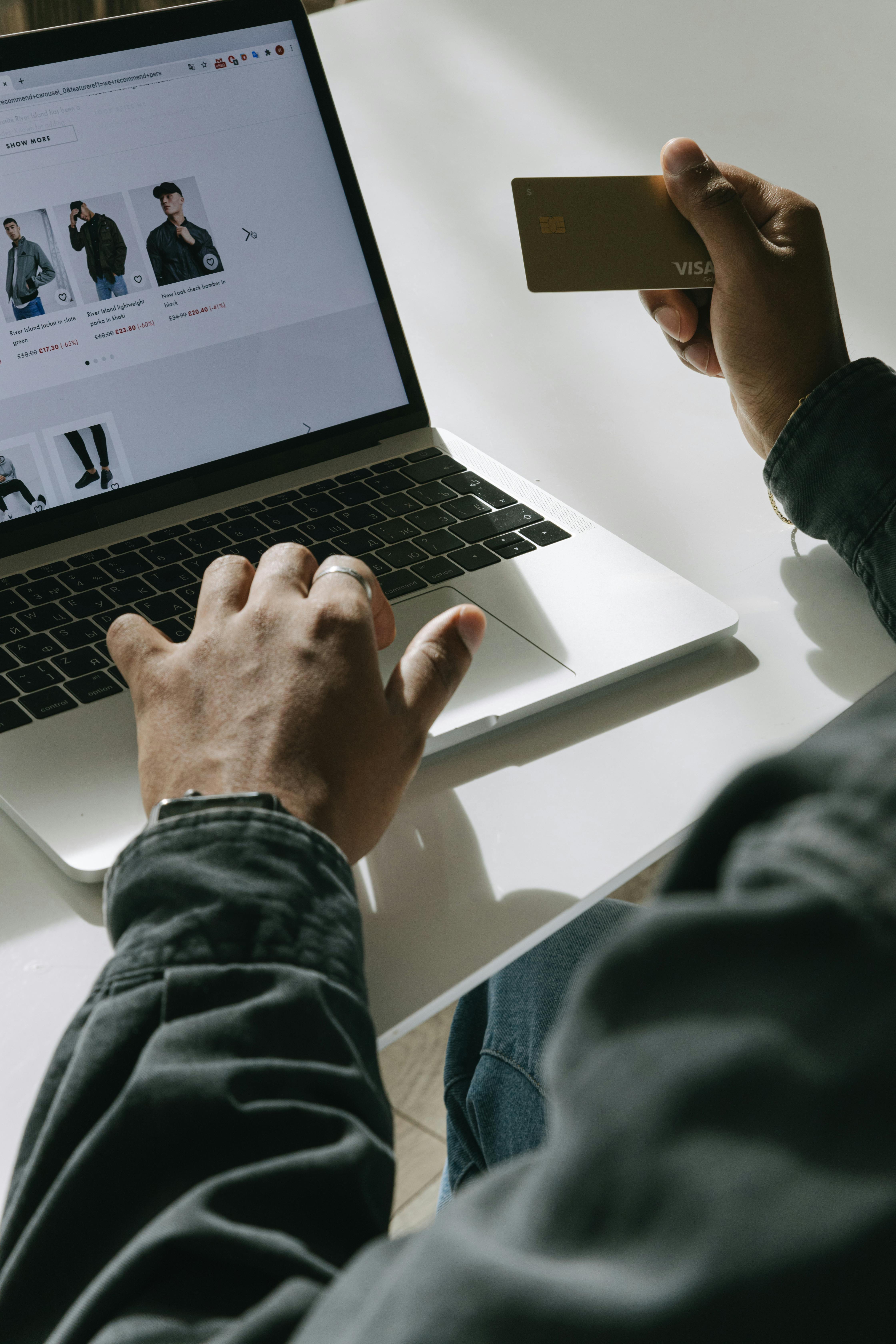 Person holding a credit card while shopping online on a laptop.