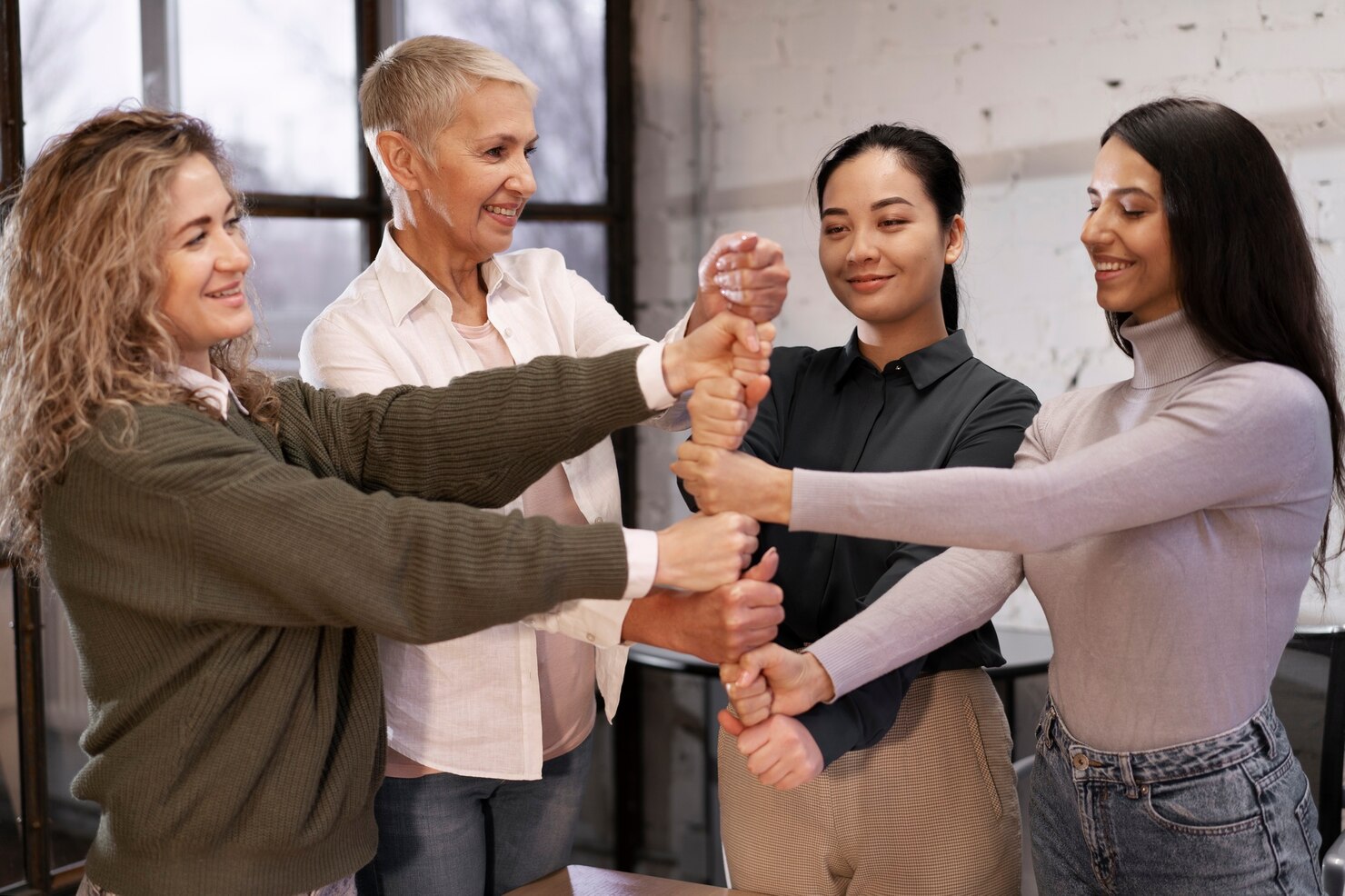 Vier diverse Menschen im Kreis, halten Hände übereinander, Team