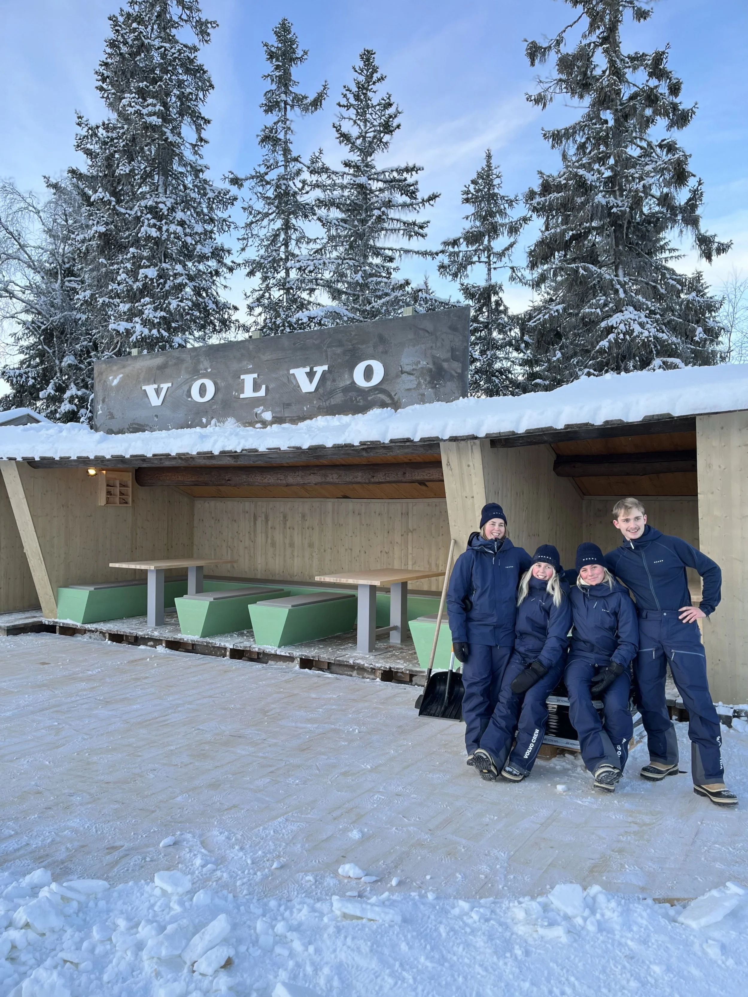 Fyra personer i Volvo-utrustning står framför en snötäckt Volvo-stuga