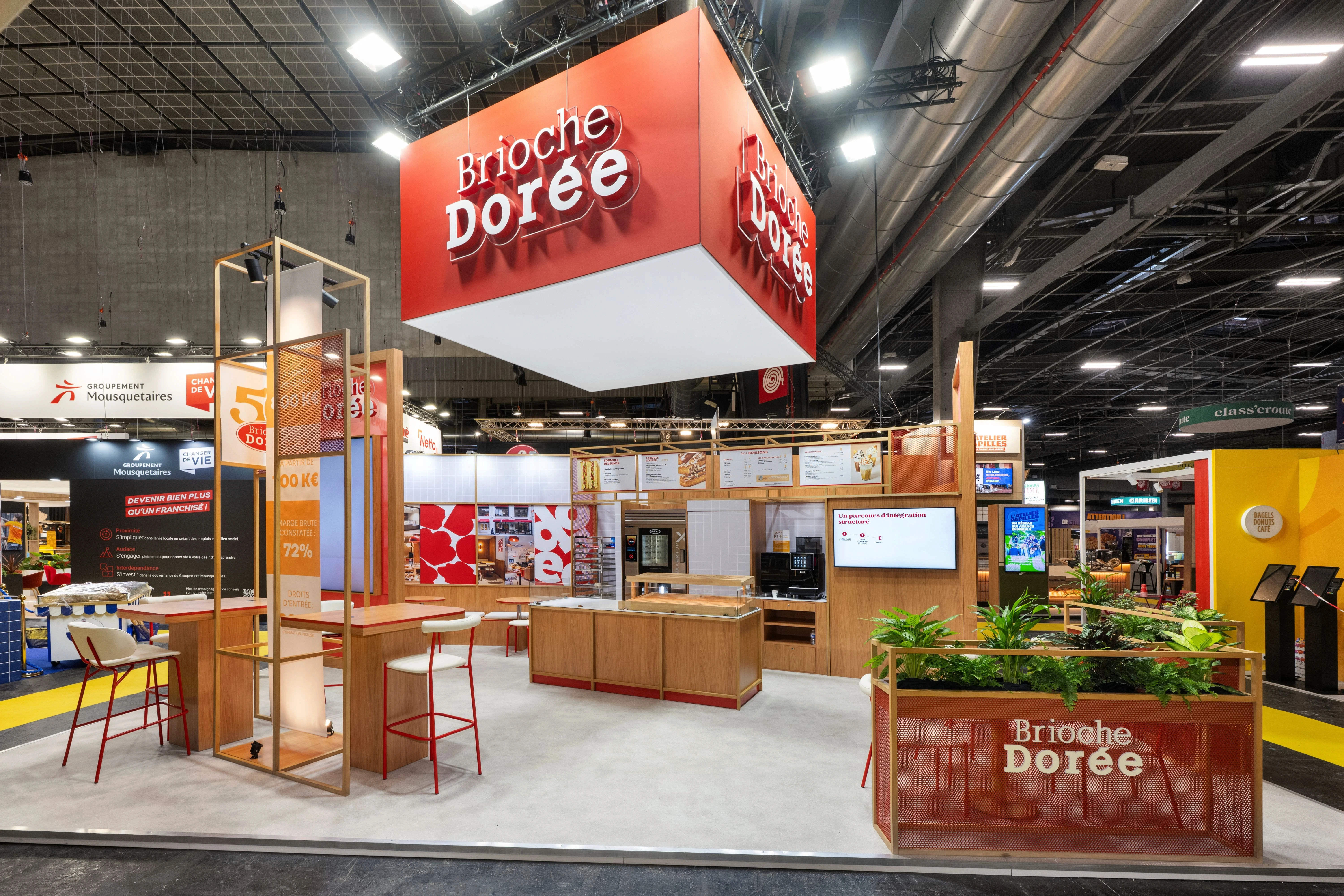 Stand Brioche Dorée conçu et réalisé par Expace pour Franchise Expo Paris 2026 – stand sur-mesure avec enseigne suspendue rouge, espace dégustation, comptoir boulangerie et tables d'accueil franchise.
