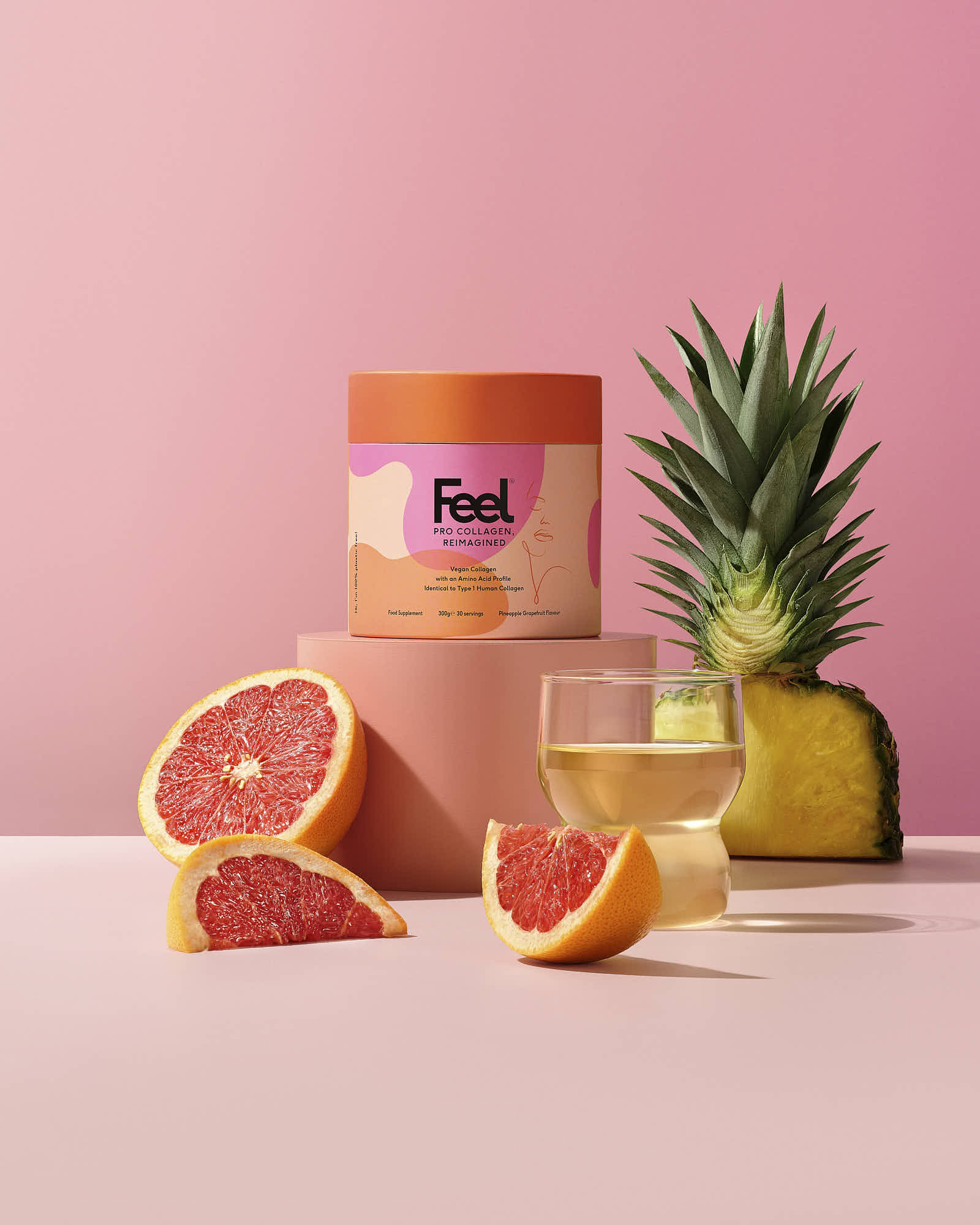 Colorful arrangement of grapefruit, lemon slices, and a pineapple beside a pink container on a pastel background.