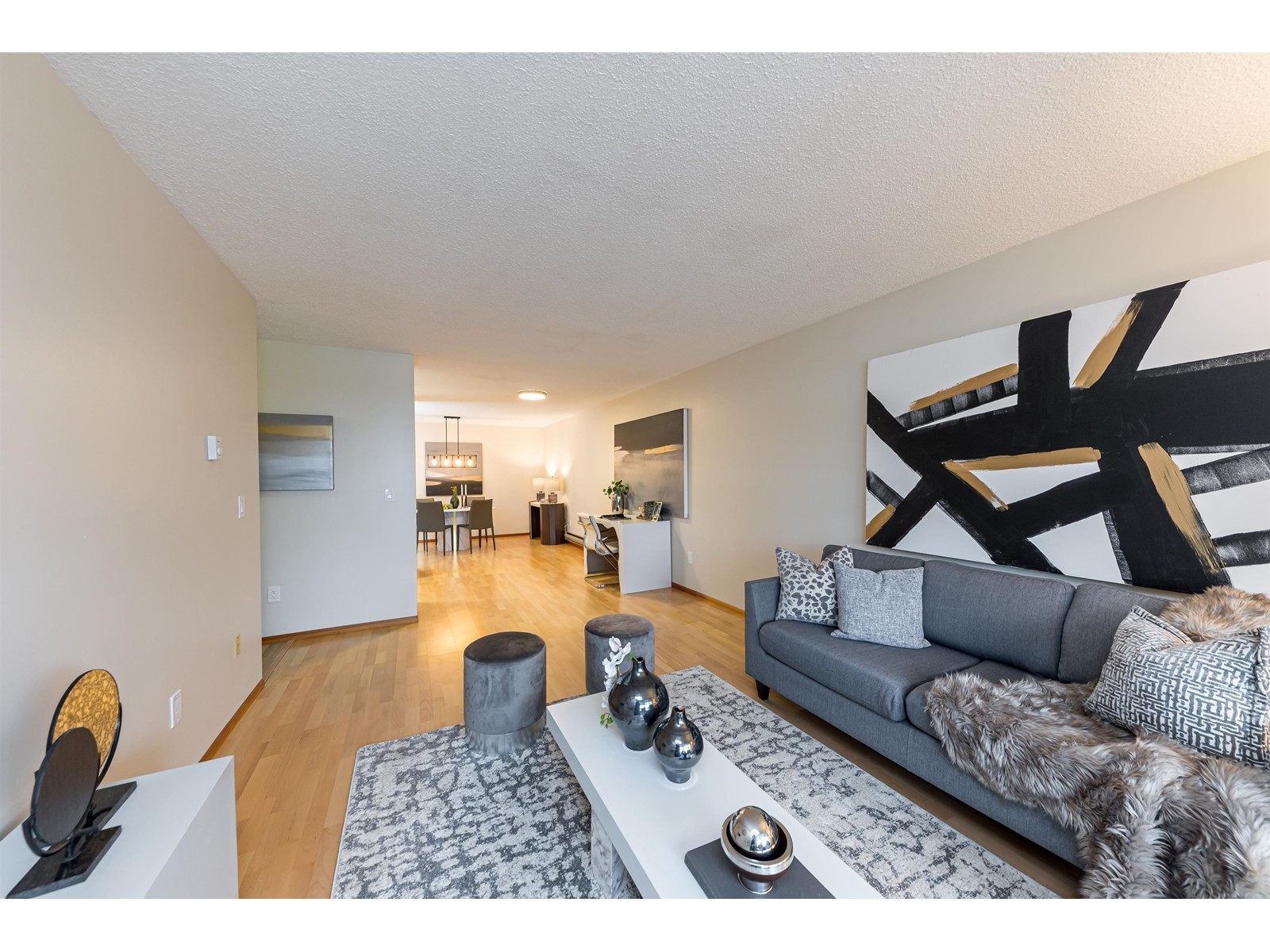 A modern living room featuring a gray sofa, abstract wall art, and wooden flooring, creating a spacious ambiance.