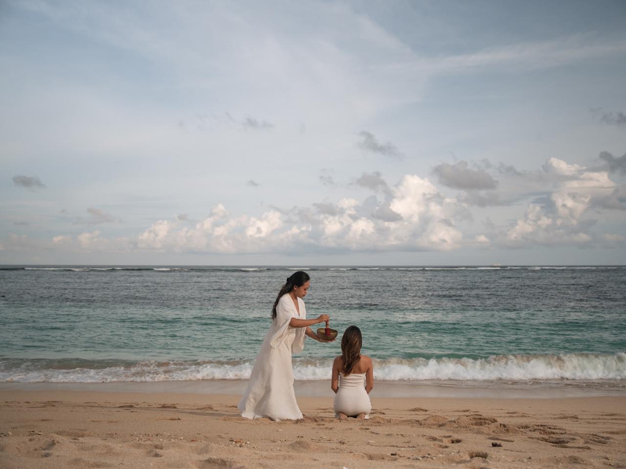 Woman practicing yoga warrior pose on a wooden platform surrounded by forested mountains in early morning light.
