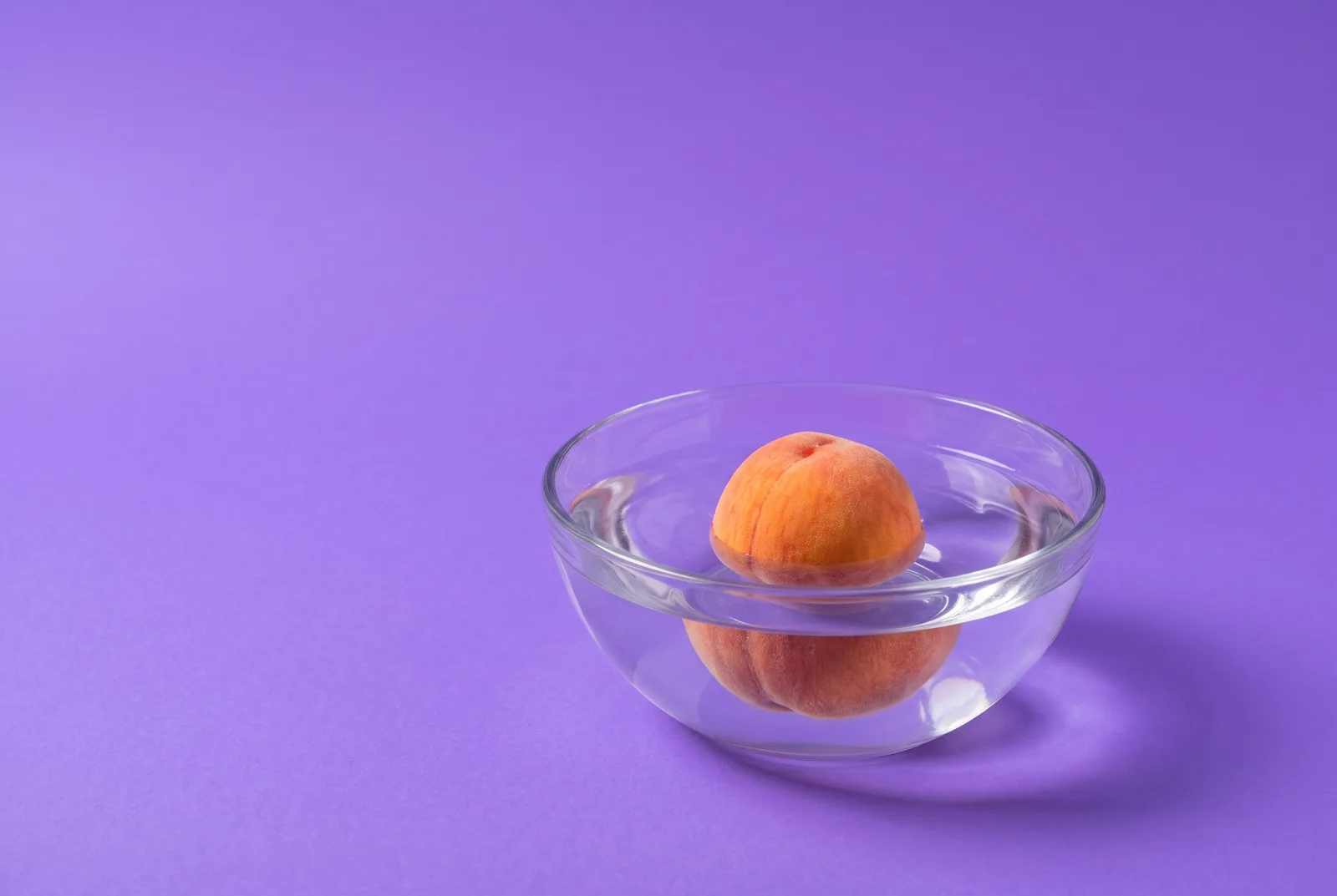 A peach floating calmly in a glass bowl of rippling water, the slow breathing step of the urge surfing technique
