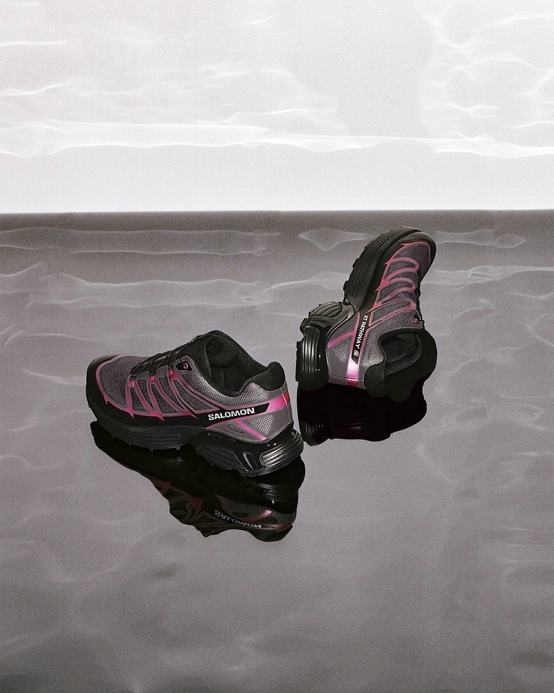 Une paire de baskets Salomon posées sur le sol, de couleur gris et rose