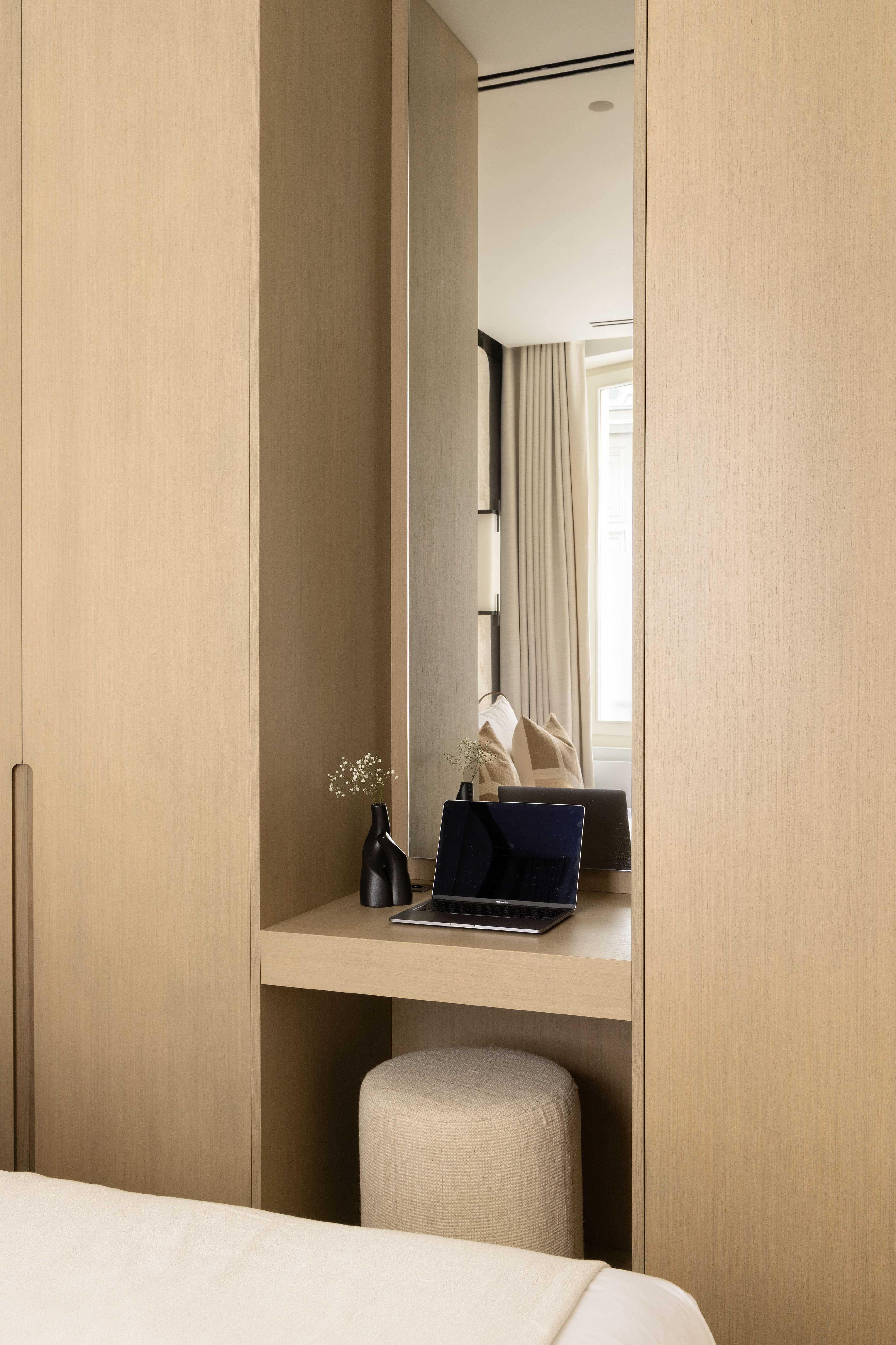 Espace bureau intégré dans la chambre avec laptop, miroir et pouf en tissu beige