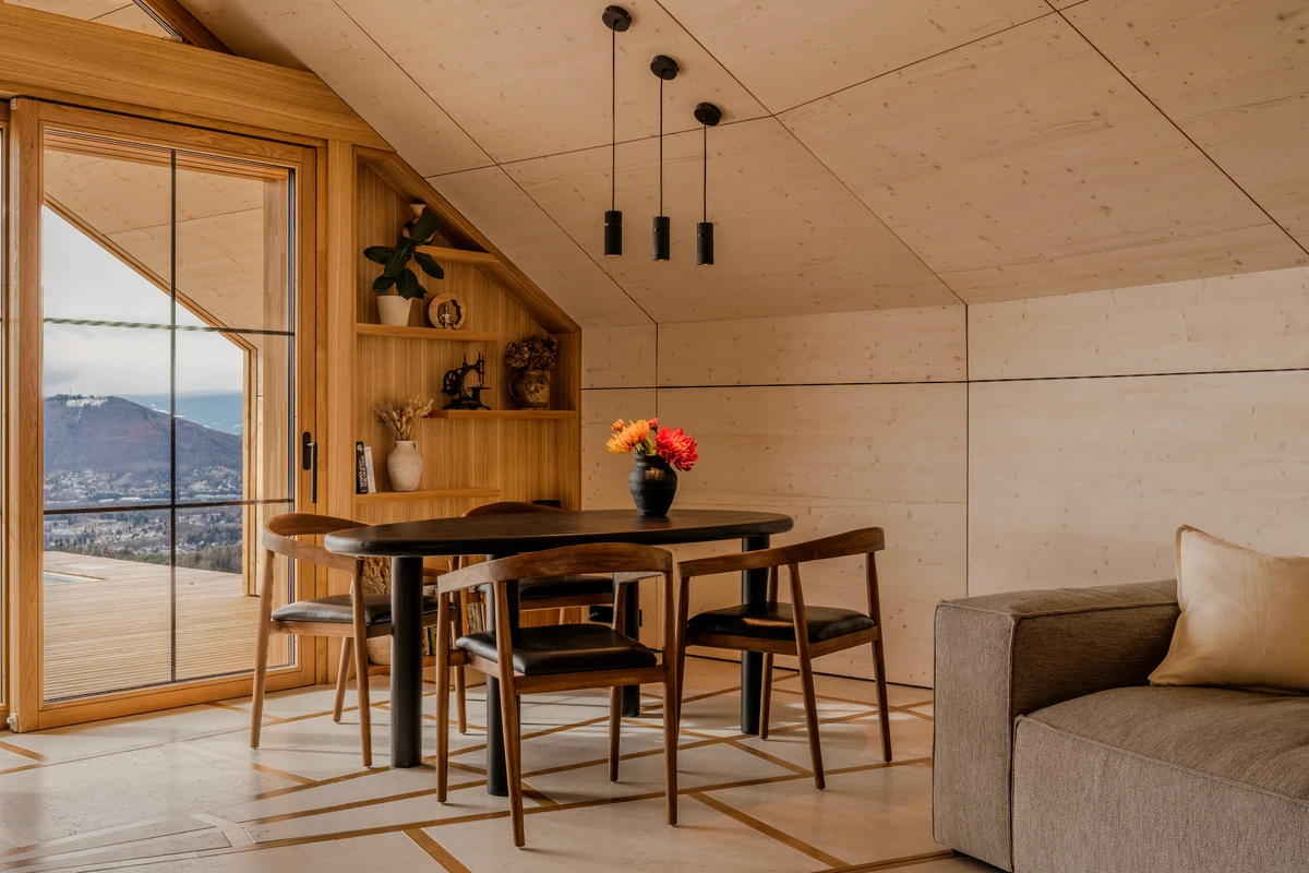 Esstisch mit sechs Stühlen und Pendelleuchten im Wohnraum mit Panoramafenster zu den Bergen