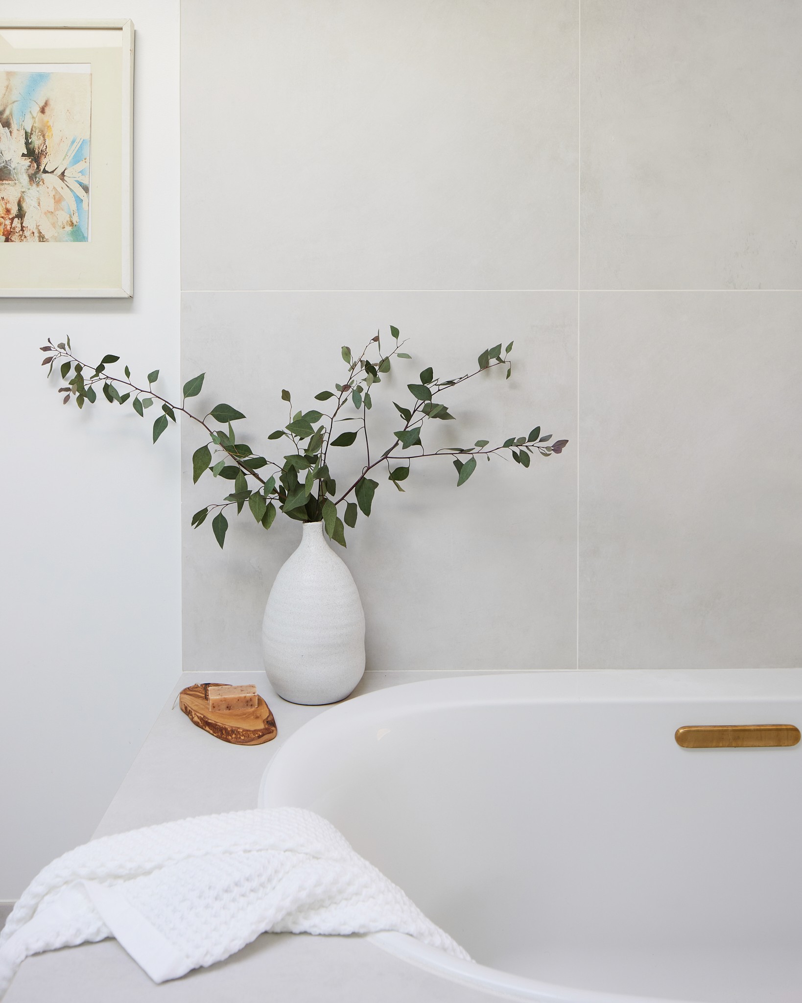 Bright master bathroom soaking tub with large white porcelain tile surrounds and bronze fixtures, with bath accessories and greenery by Jubilee Interiors in Los Angeles, California