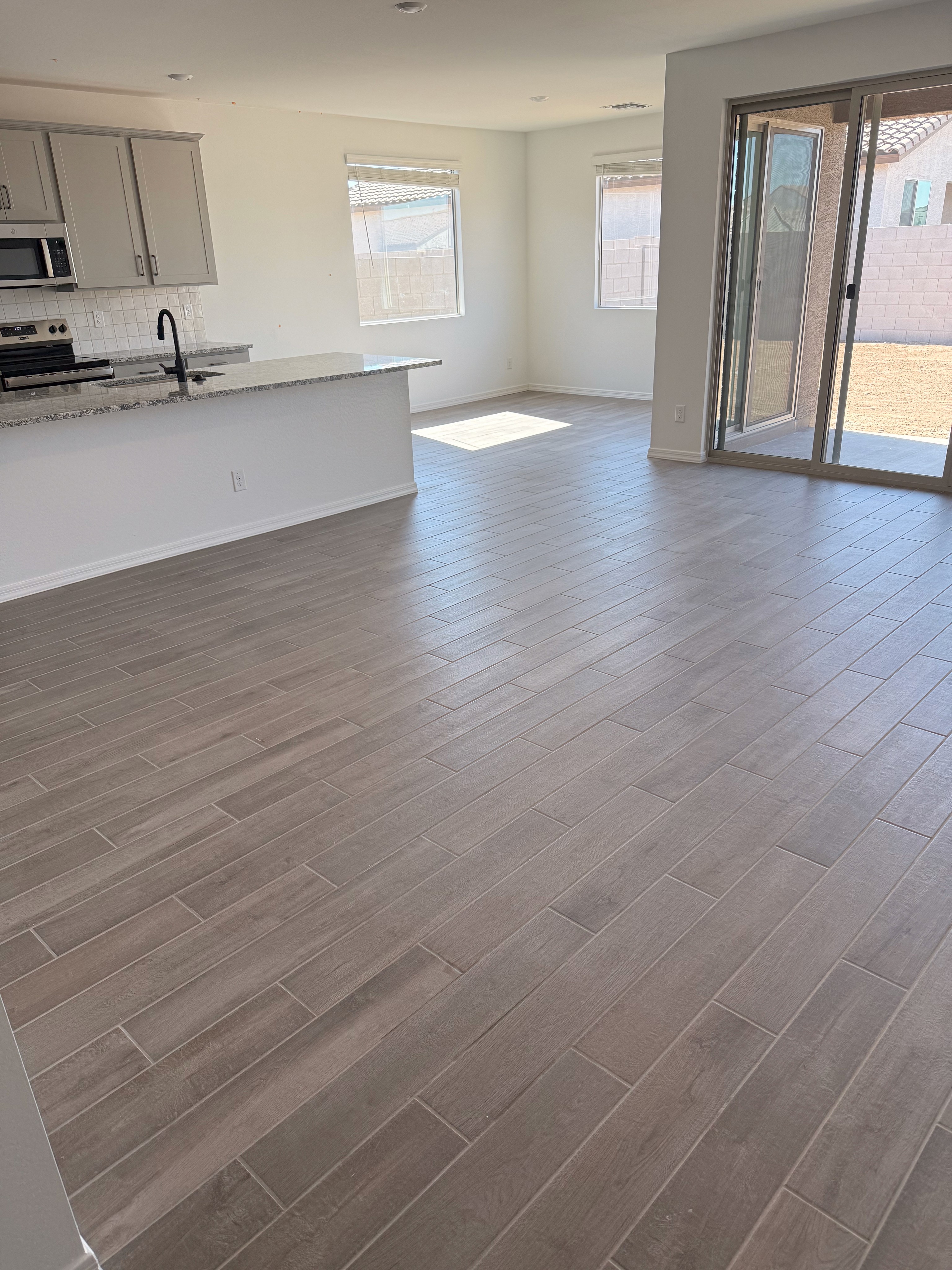 Modern open-plan kitchen and living area with wood-look tiles, kitchen island, and large sliding glass doors to backyard.