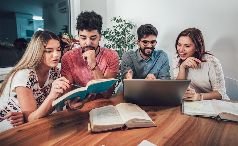 A group of students sitting around the table studying, displaying a study group. 