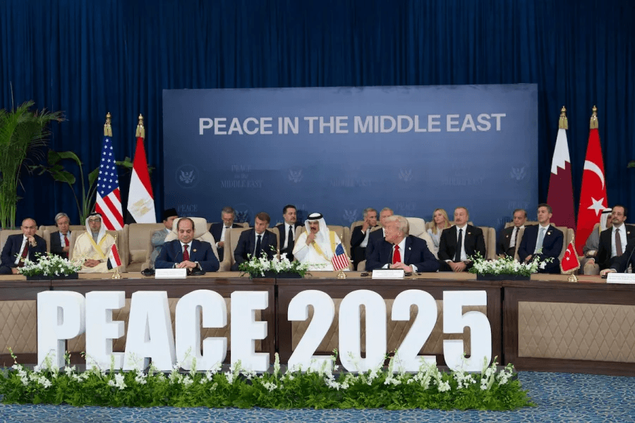 A circle of people sitting cross-legged, meditating with hands in a prayer position. Soft, warm lighting.