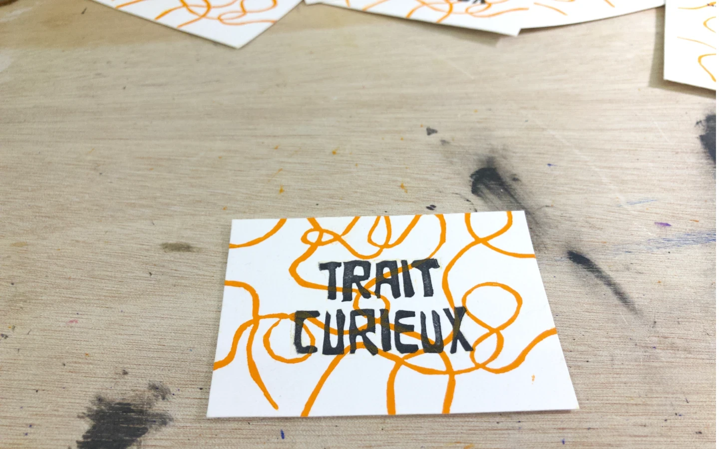 Carte de visite complète du projet Trait Curieux, imprimée en linogravure et caractères mobiles, posée sur l'établi de l'atelier.