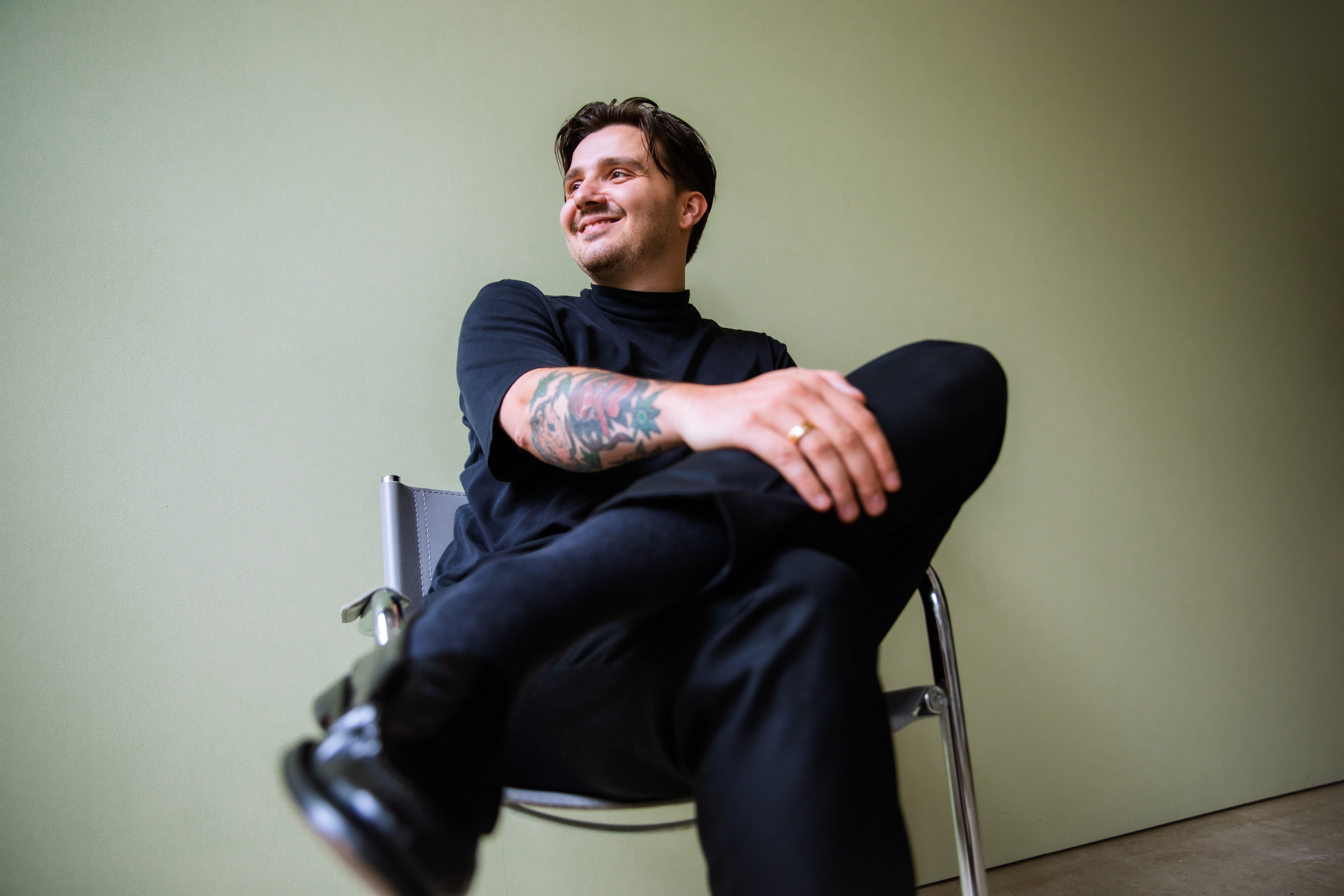 緑の背景の前に座っている、黒い服を着た笑顔の人物のポートレート