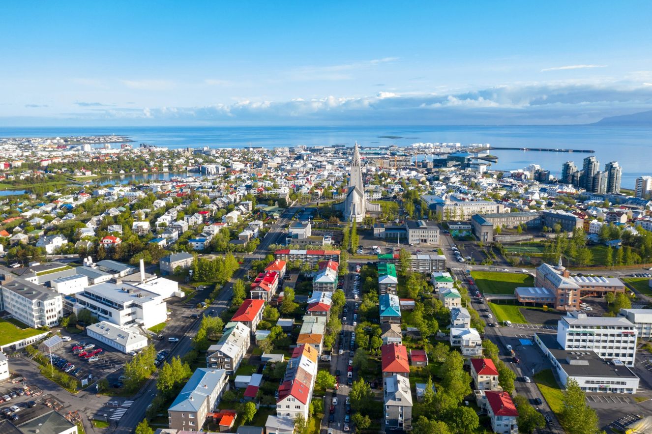 Drone view of Reykjavík featuring Hallgrímskirkja, colorful neighborhoods, and Faxaflói Bay.