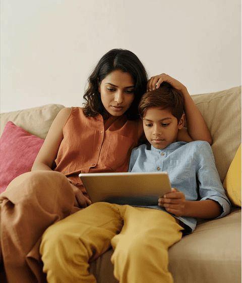 A mother and her son are sitting together, using a tablet to work on homework