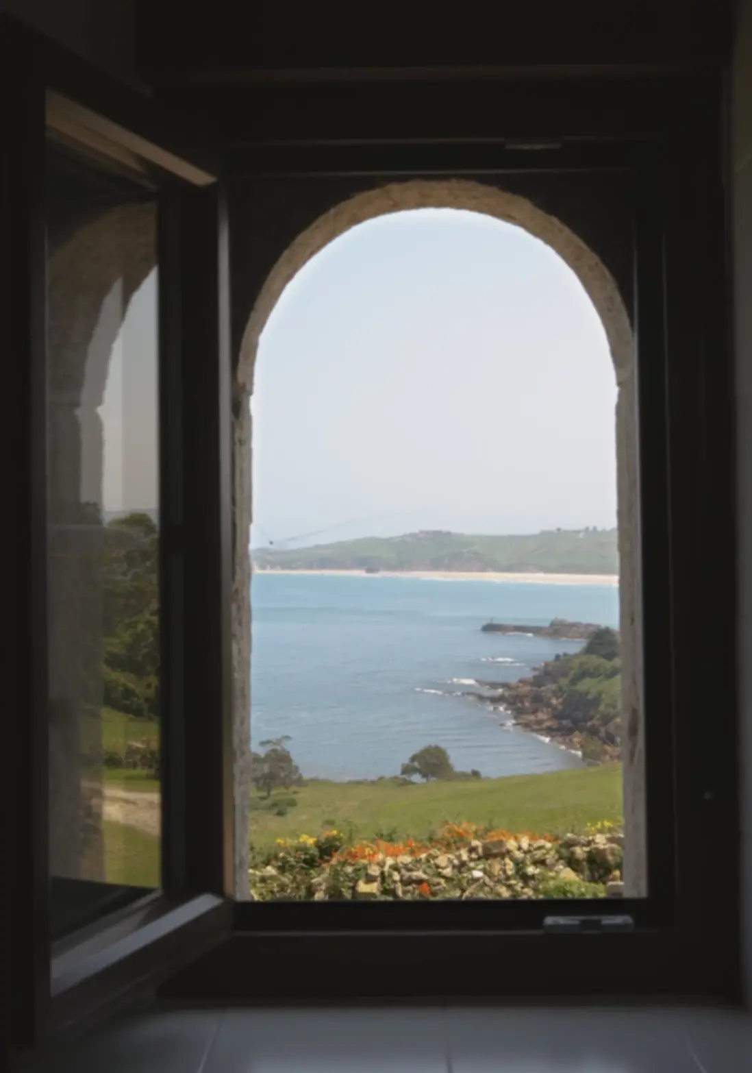 ventana que da al mar tras un prado