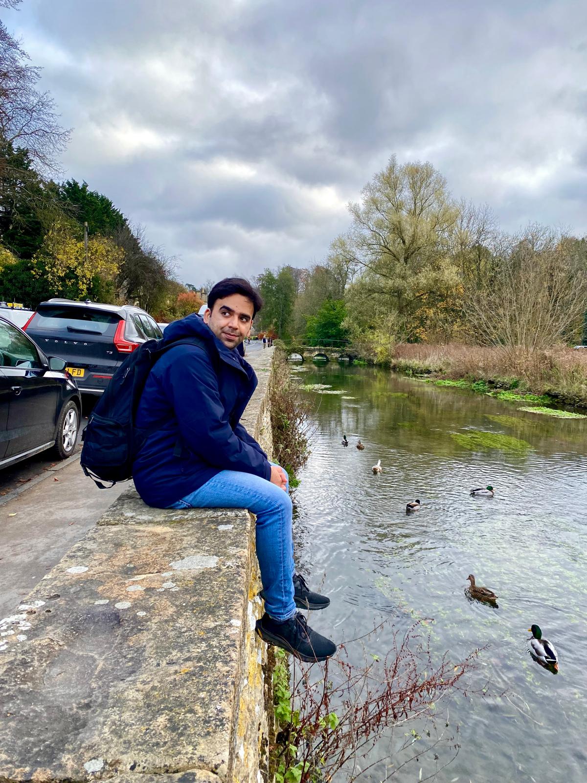 A photo of myself sitting on the side of a canal. Next to parked cars.
