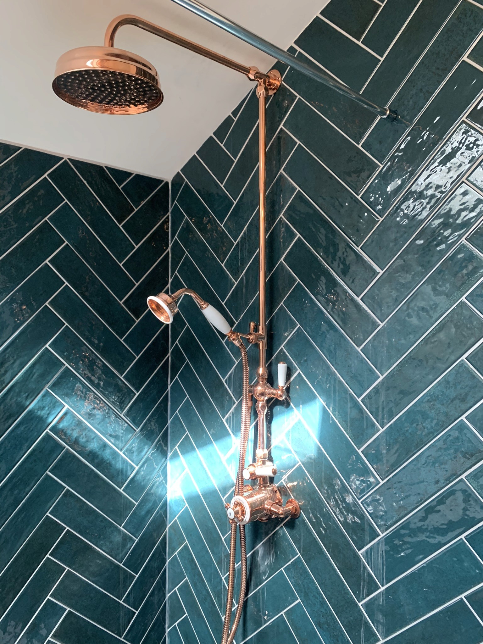 Copper shower fittings in green herringbone tile shower enclosure