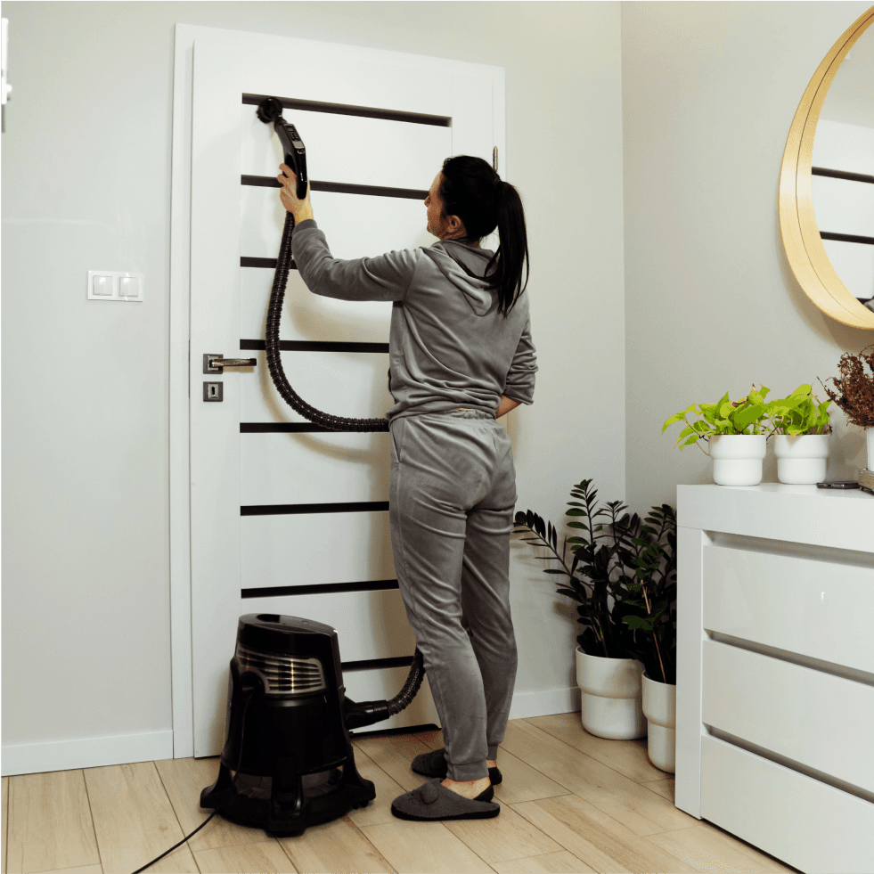 Woman cleaning a black metal shelf with a vacuum cleaner in a modern room.