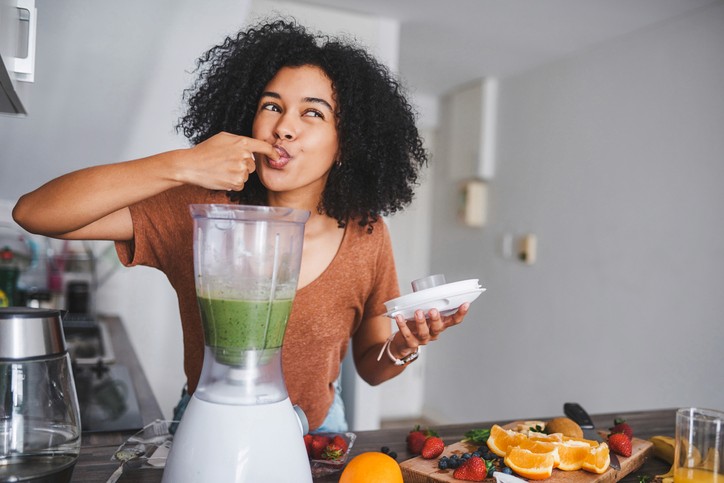 happy woman tasting green smoothie from blender