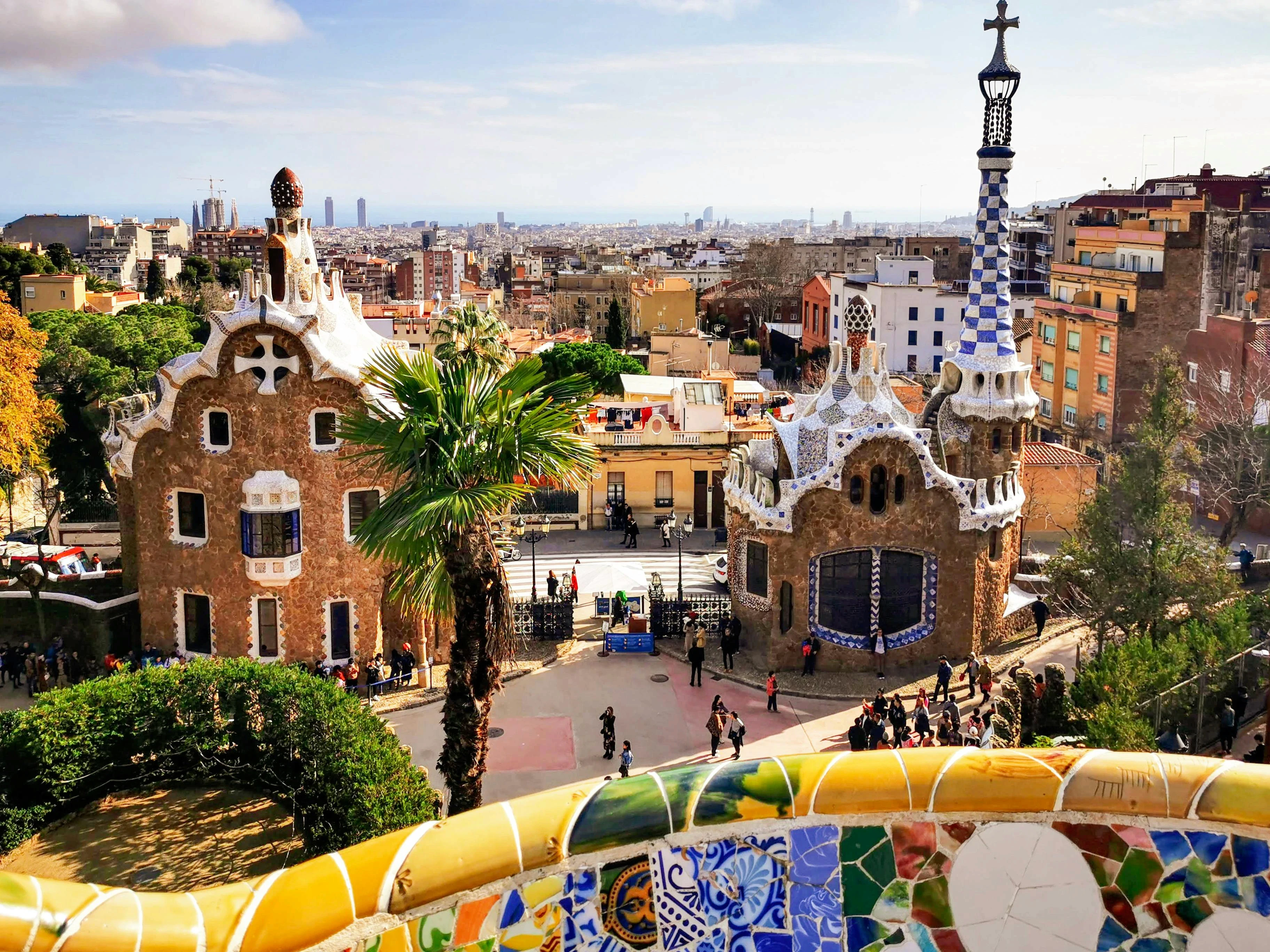 A panoramic sunrise view of Park Güell with the Mediterranean Sea in the distance.