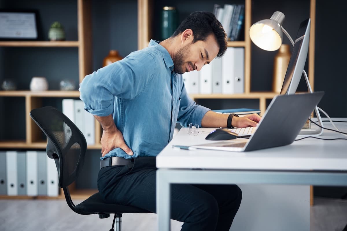 Mann mit Rückenschmerzen der am Schreibtisch sitzt