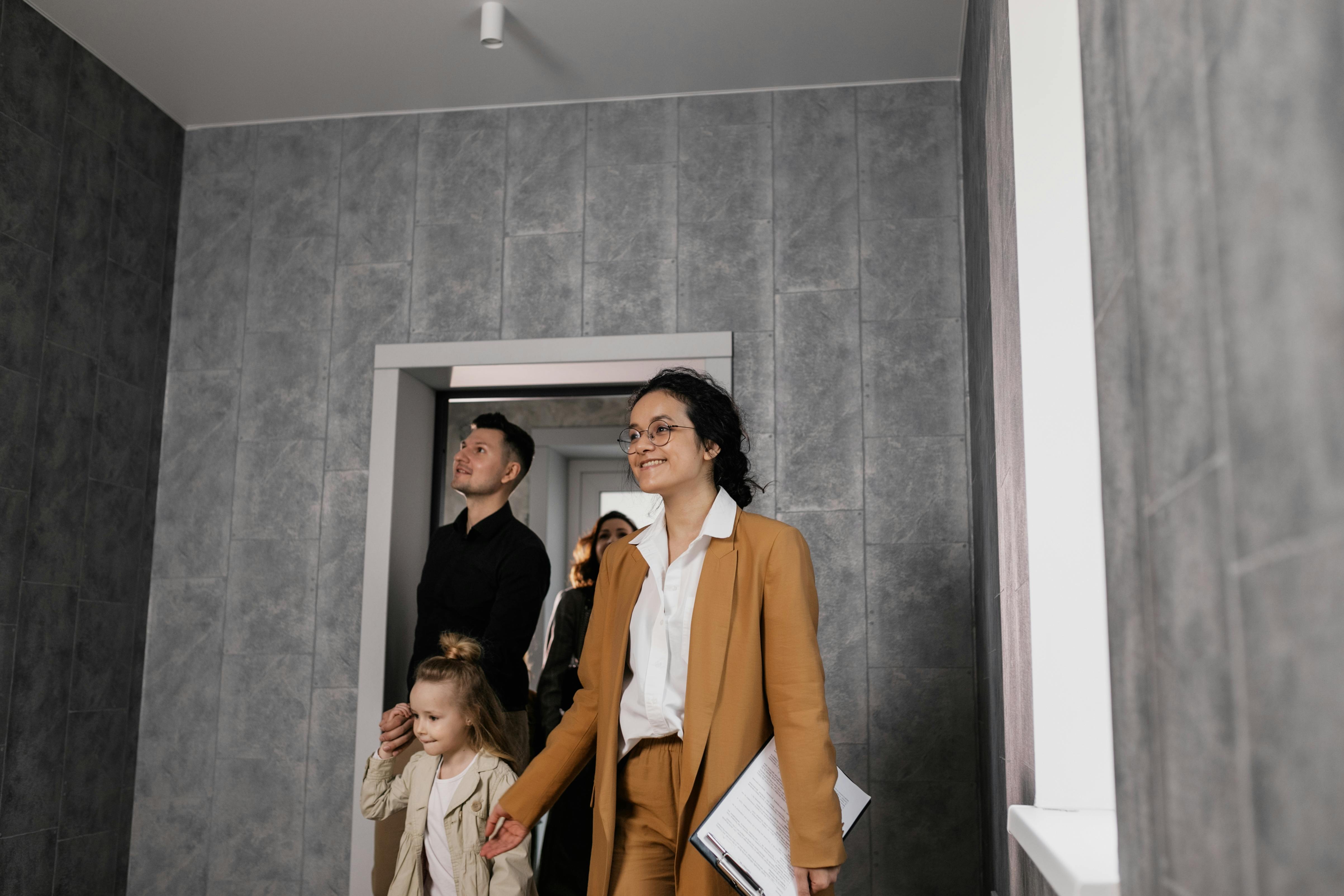 A smiling real estate agent showing a young newcomer family a modern Canadian apartment during an in-person viewing.