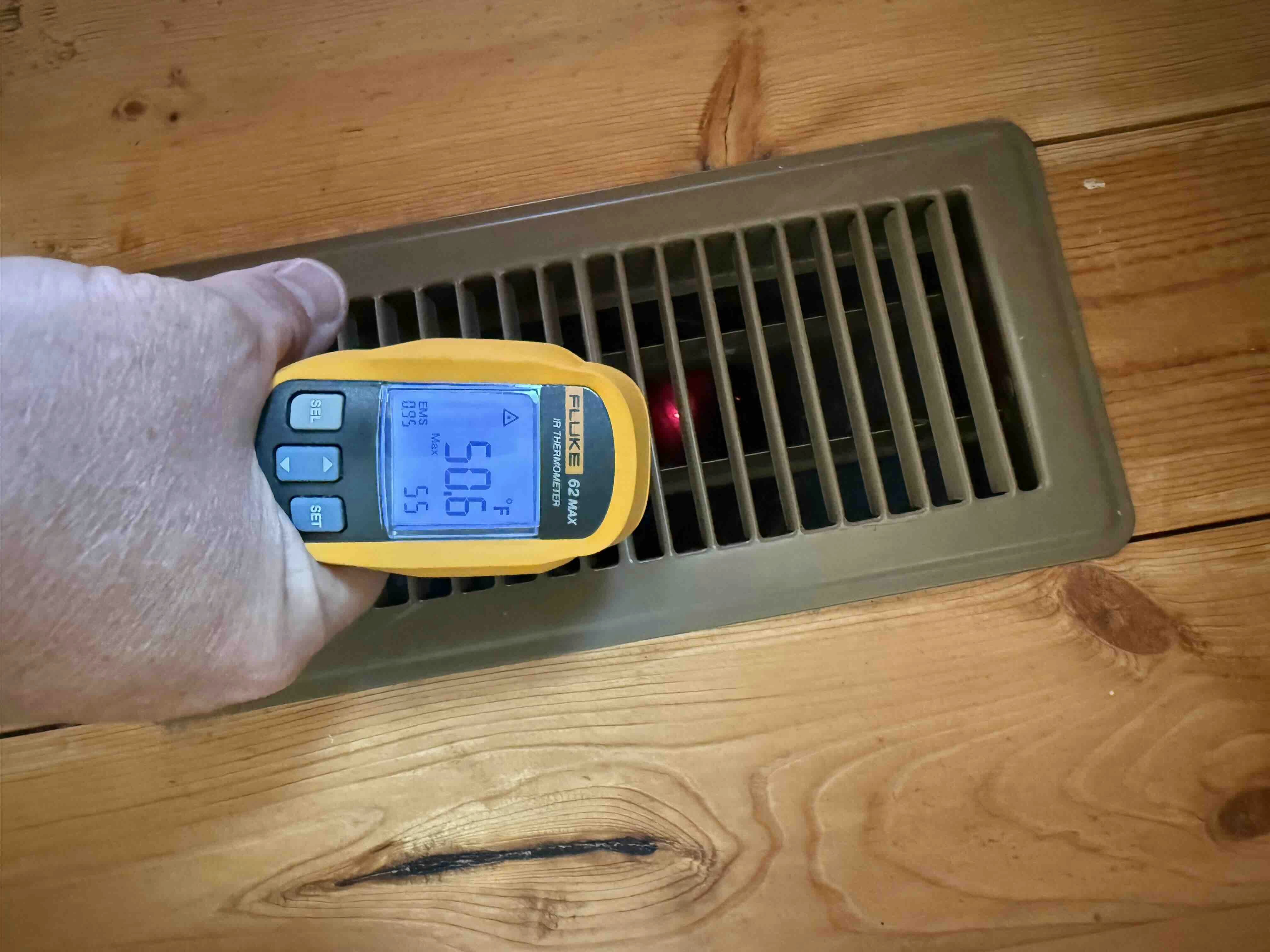 An infrared thermometer reading the temperature at a floor supply register.