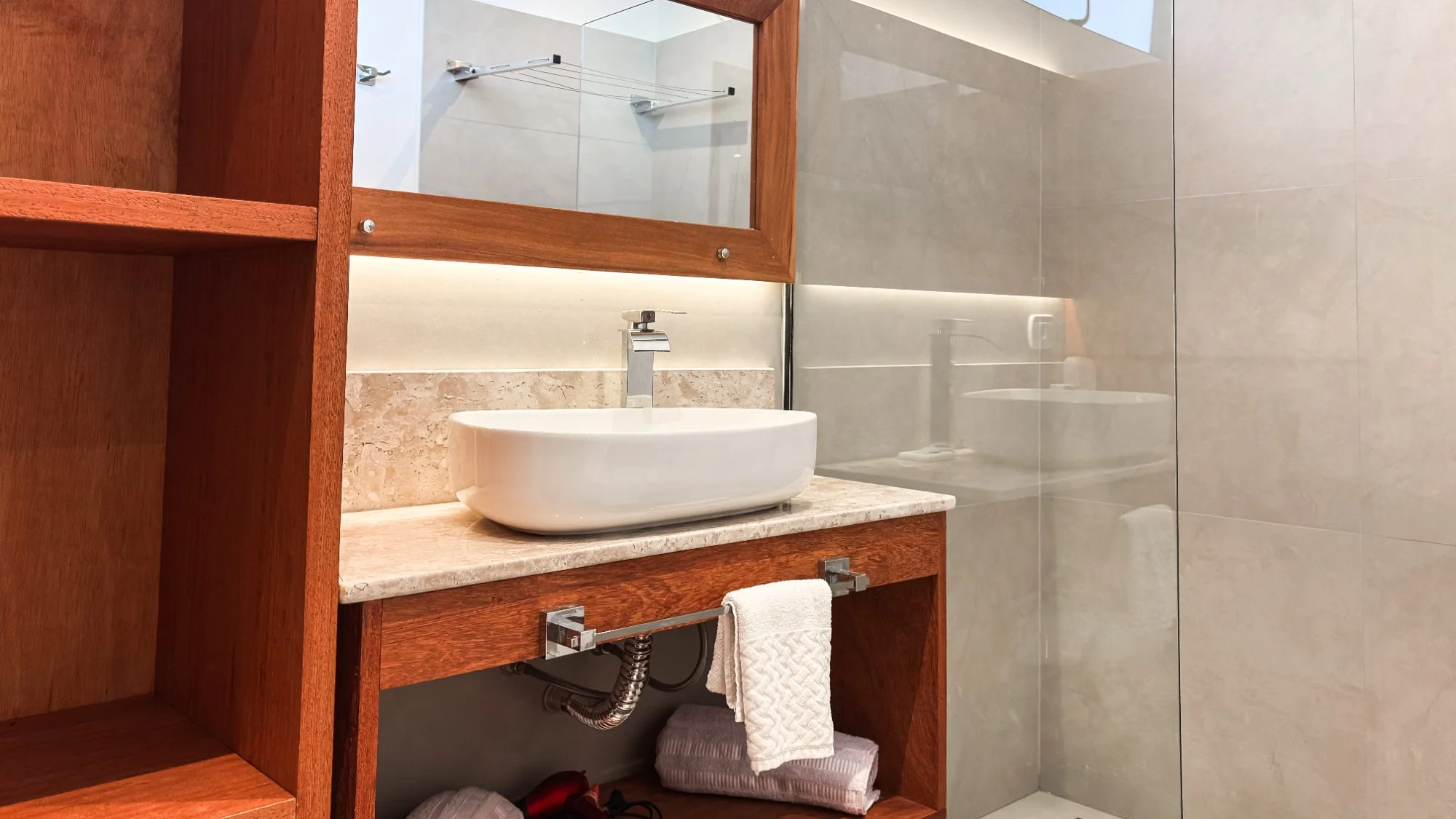 Bathroom vanity detail with white vessel sink, marble top, wooden frame, and glass shower screen