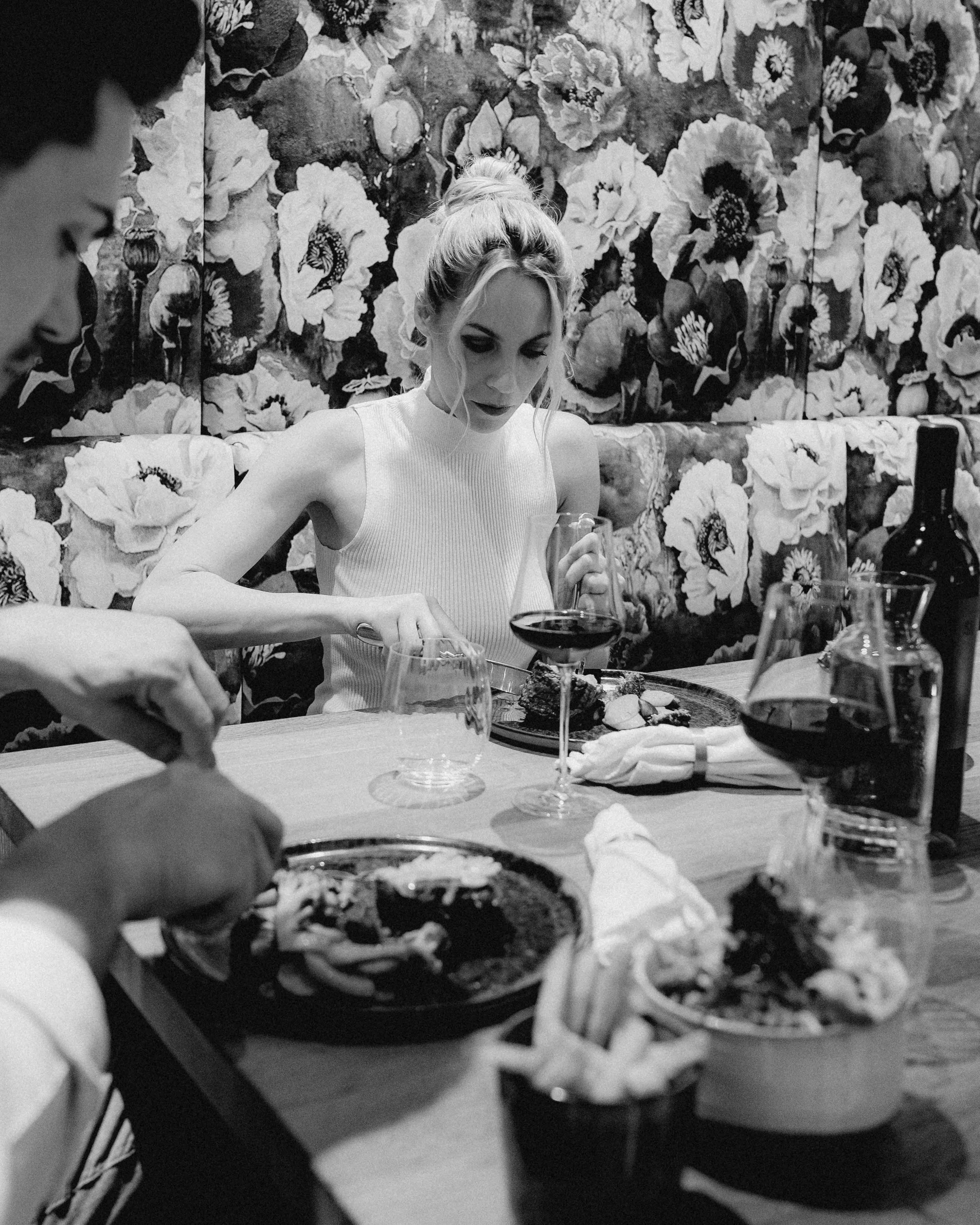 A woman sewing at a table, surrounded by people in a crowd, in a black and white photograph.