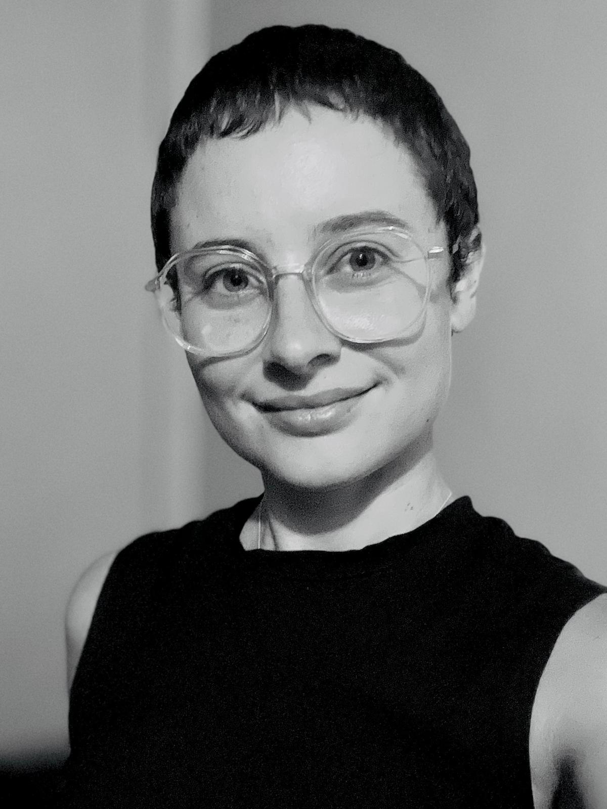 Retrato en blanco y negro de mujer con pelo muy corto oscuro, gafas transparentes y camisa negra