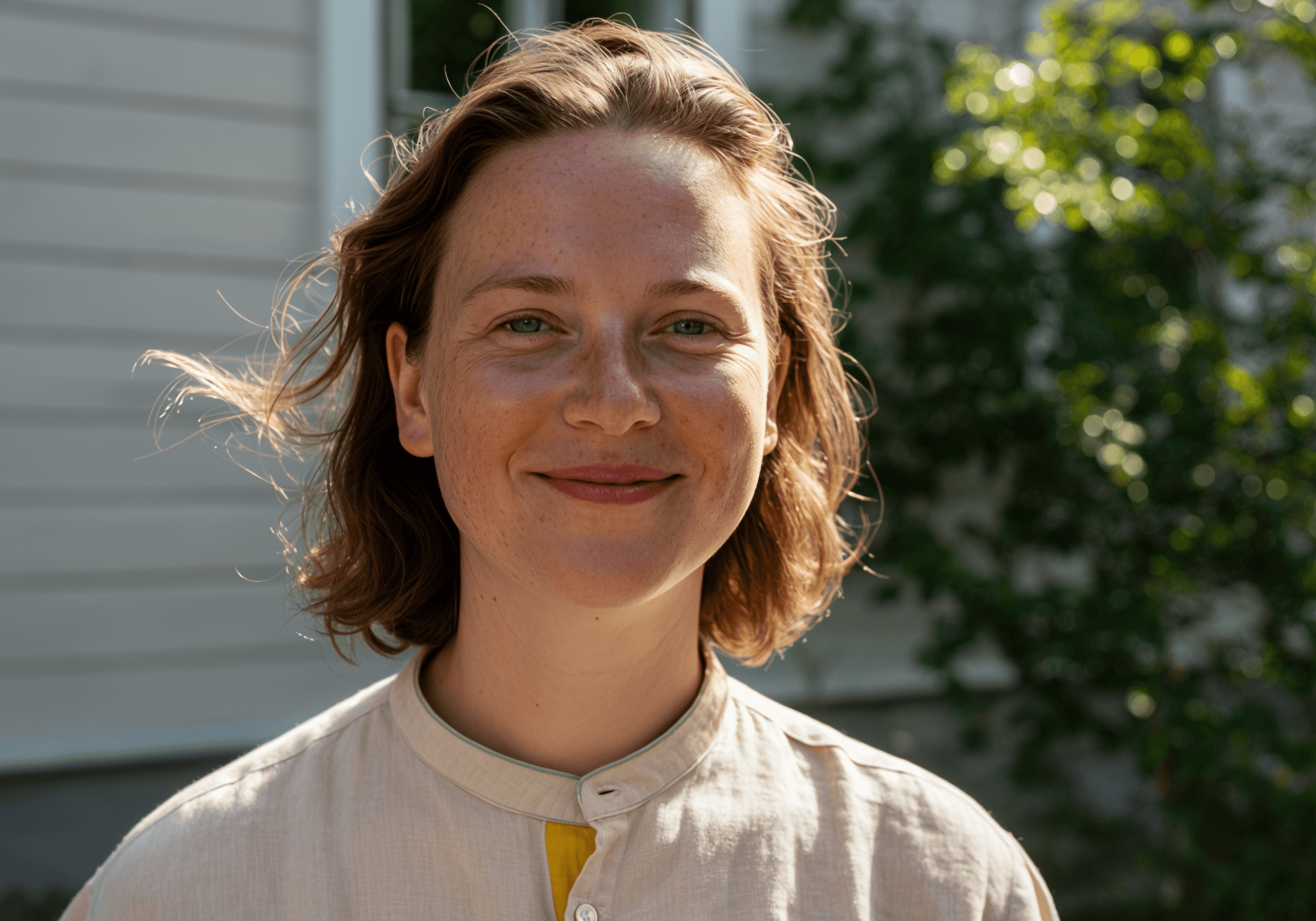 Smiling woman with short brown hair poses for a headshot in sunlight. She wears a beige shirt and has a kind expression.