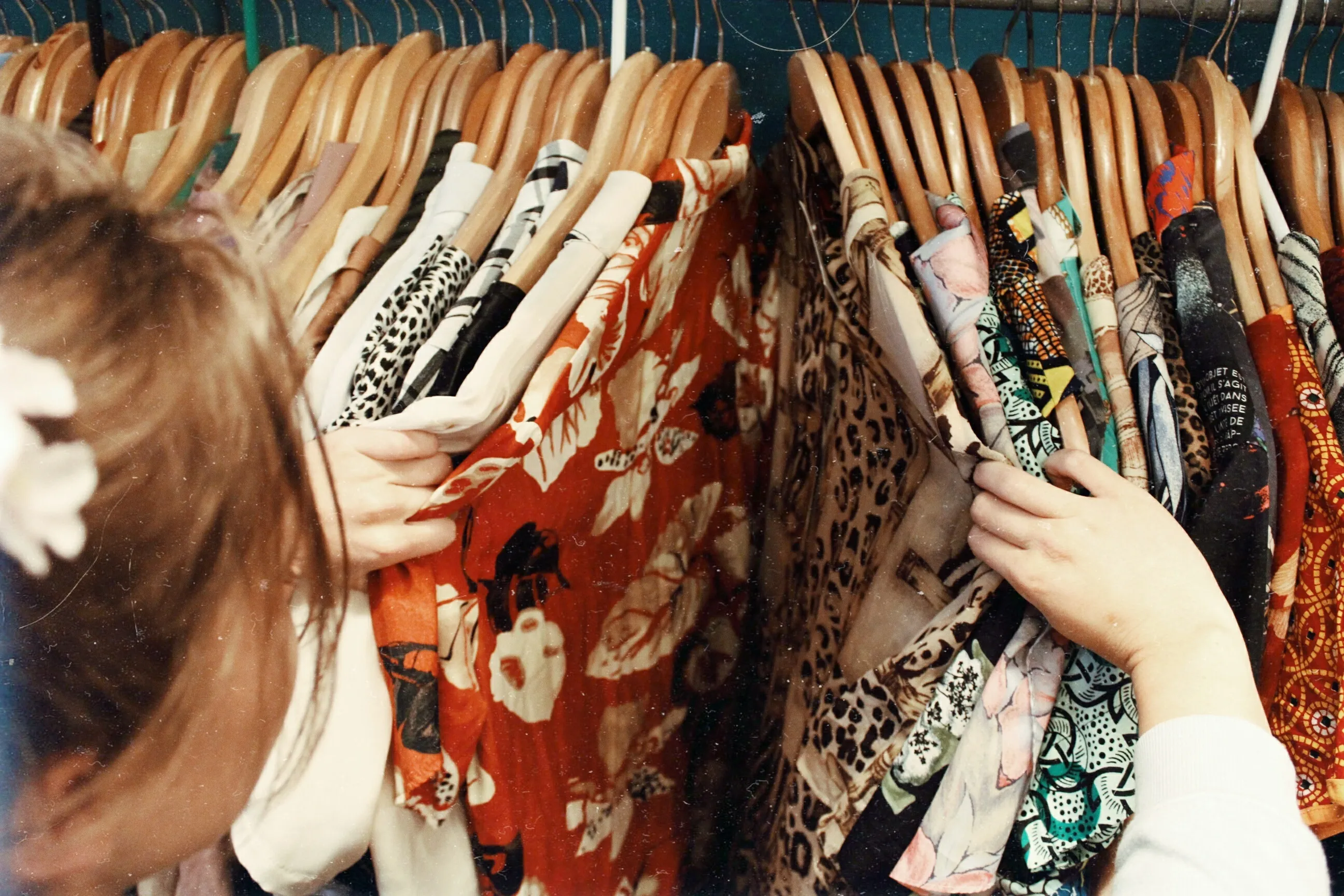 Person browsing colorful patterned clothes on a rack with wooden hangers in a boutique or wardrobe