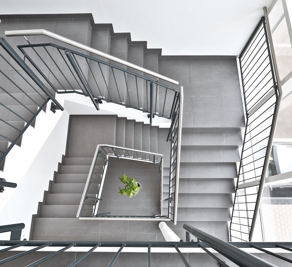 Moderne Treppenhausarchitektur mit grauen Stufen, Metallgeländern und einer Pflanze in der Mitte.