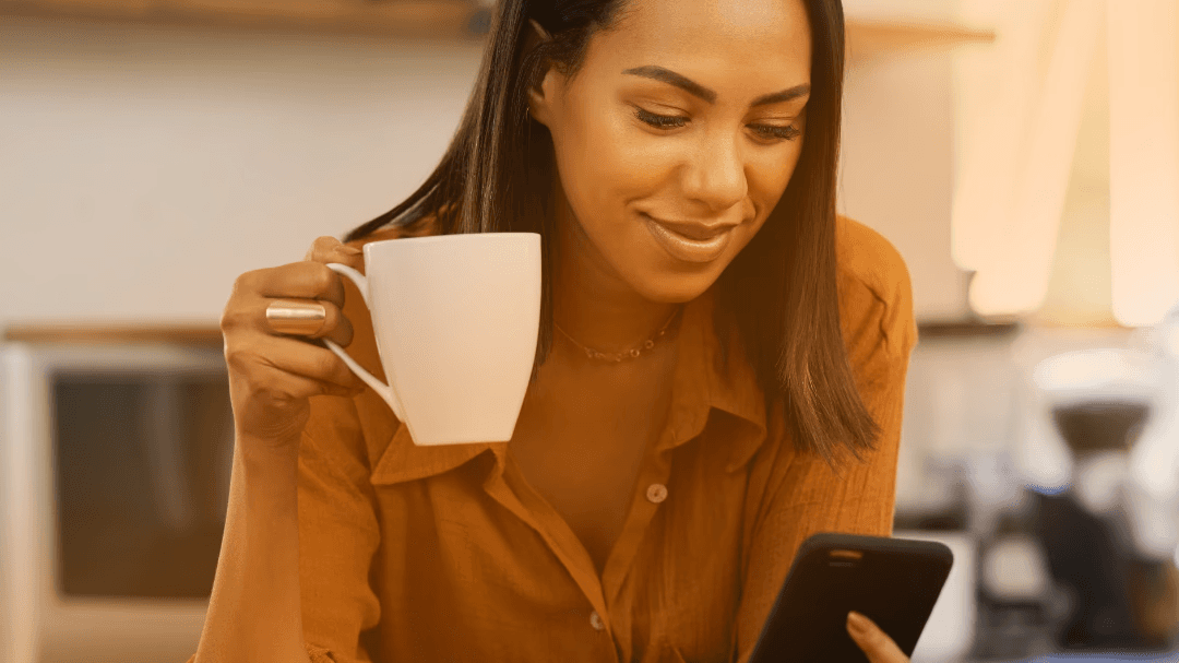 Smiling woman with her phone in her hand drinking coffee